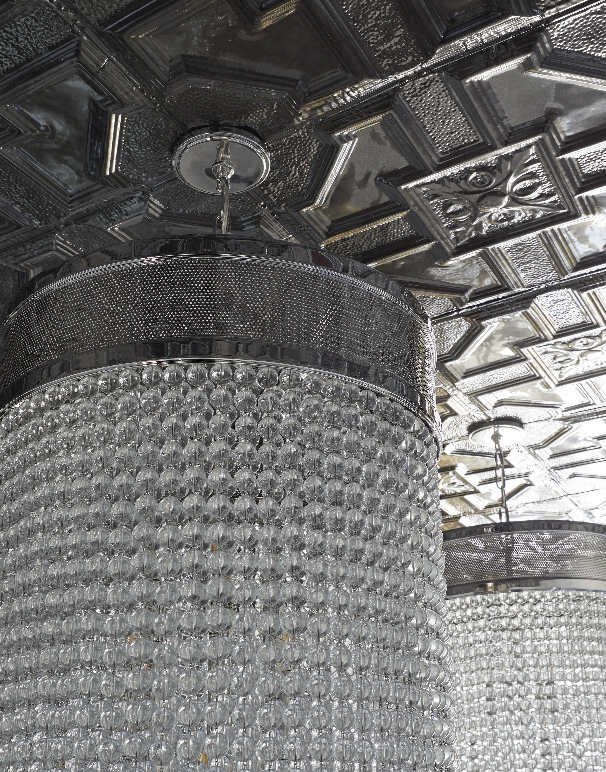 Close-up of a decorative ceiling with a shiny, metallic grid pattern and a chandelier with numerous small clear glass spheres.