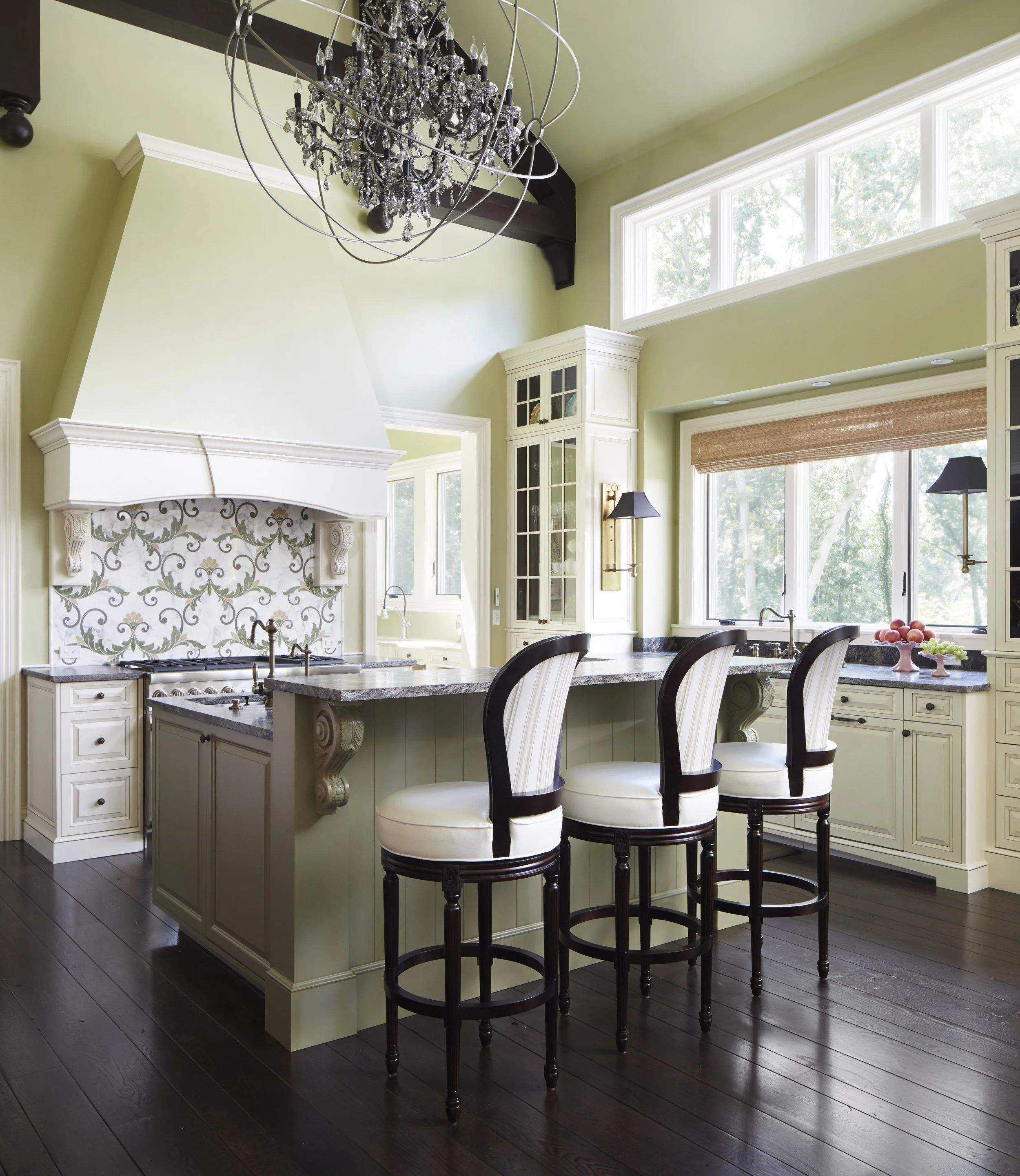 Kitchen with a white island, dark wood chairs, large windows, and a chandelier.
