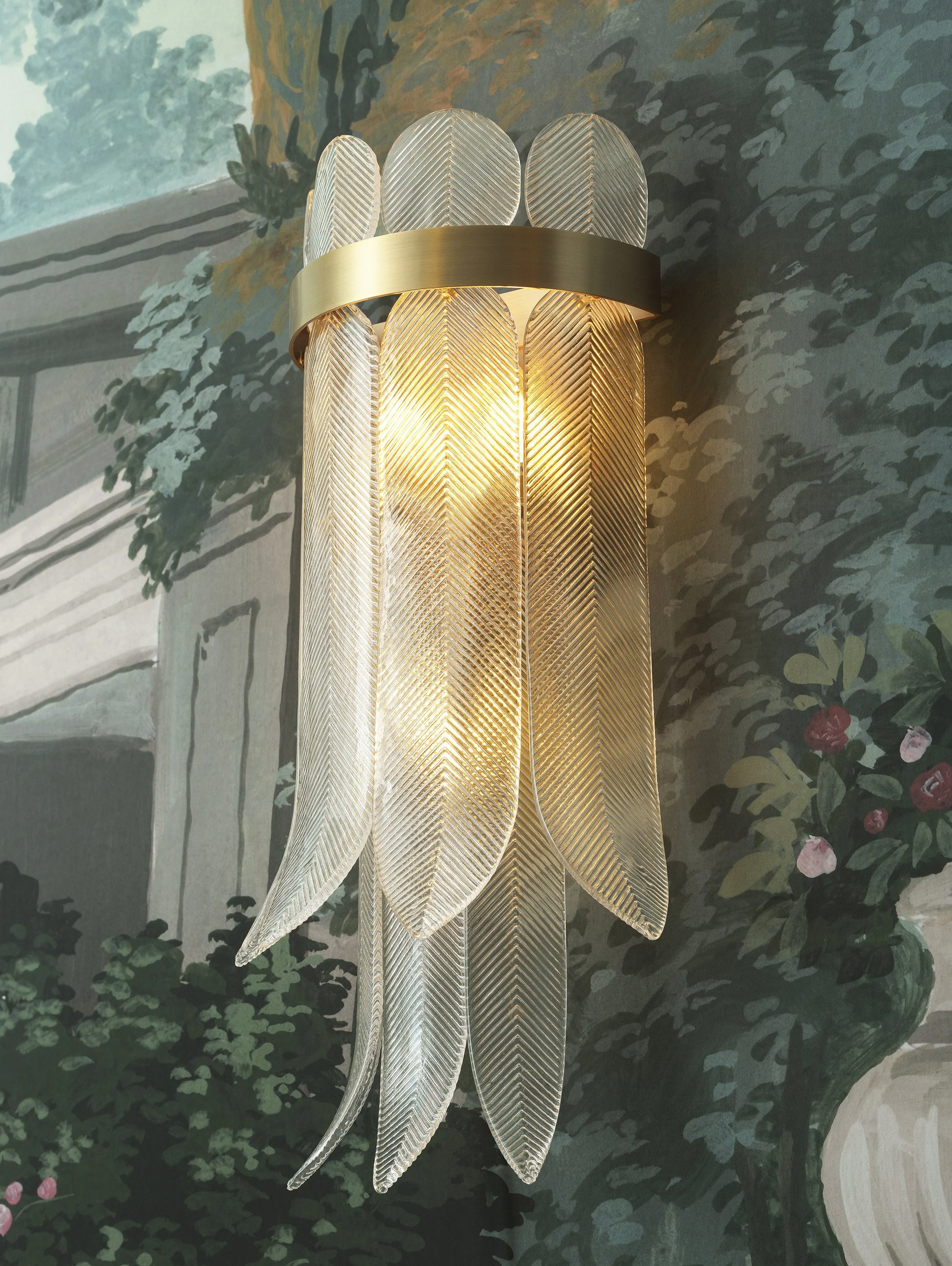 A modern chandelier with clear textured glass leaf-shaped panels and a gold band, hanging in front of a dark floral-patterned wallpaper.