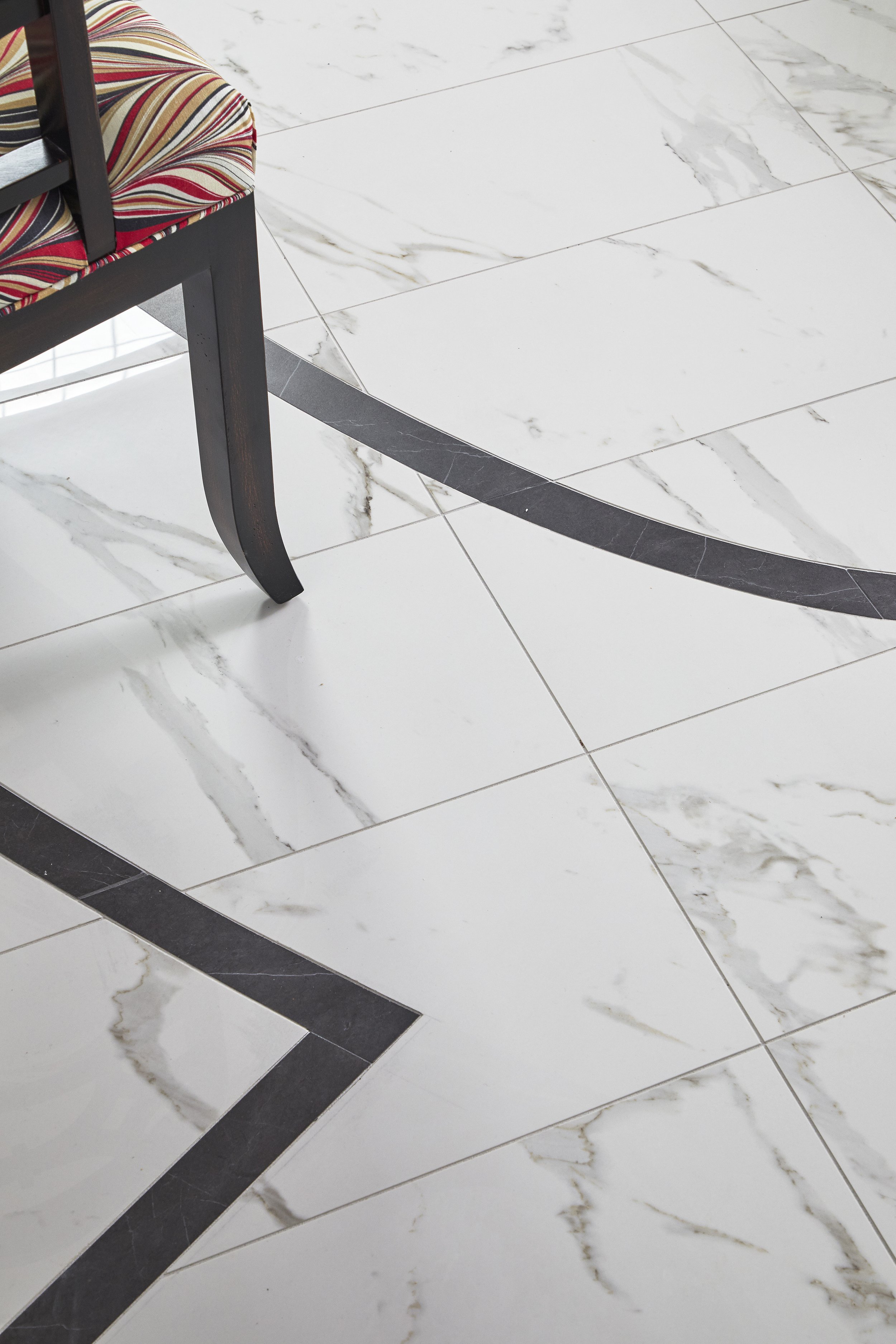 Part of a chair with a striped cushion and dark wooden frame on a white marble tiled floor.