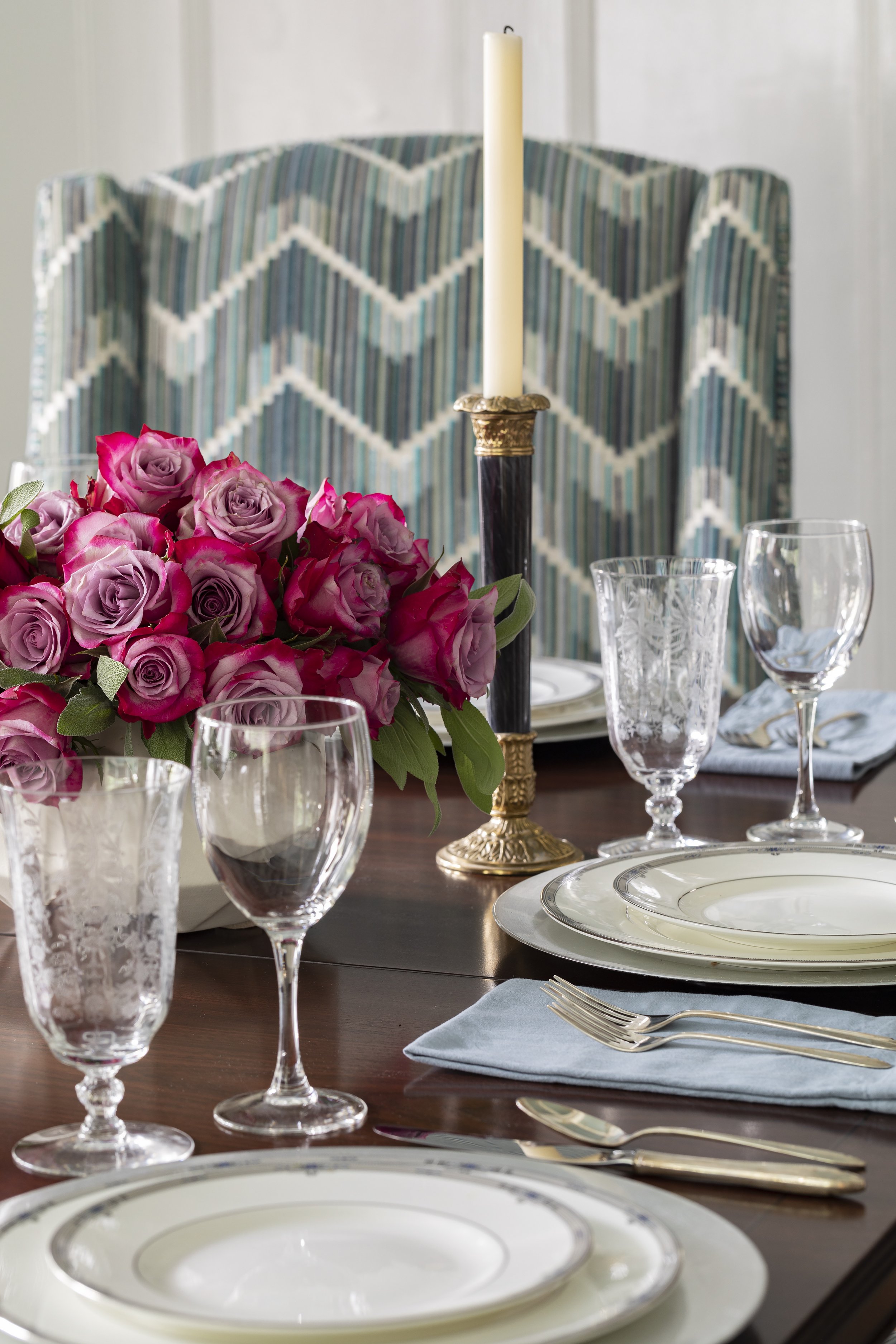 Elegant dining table setting with floral centerpiece, plates, wine glasses, and cutlery, with a tall candlestick in the background.
