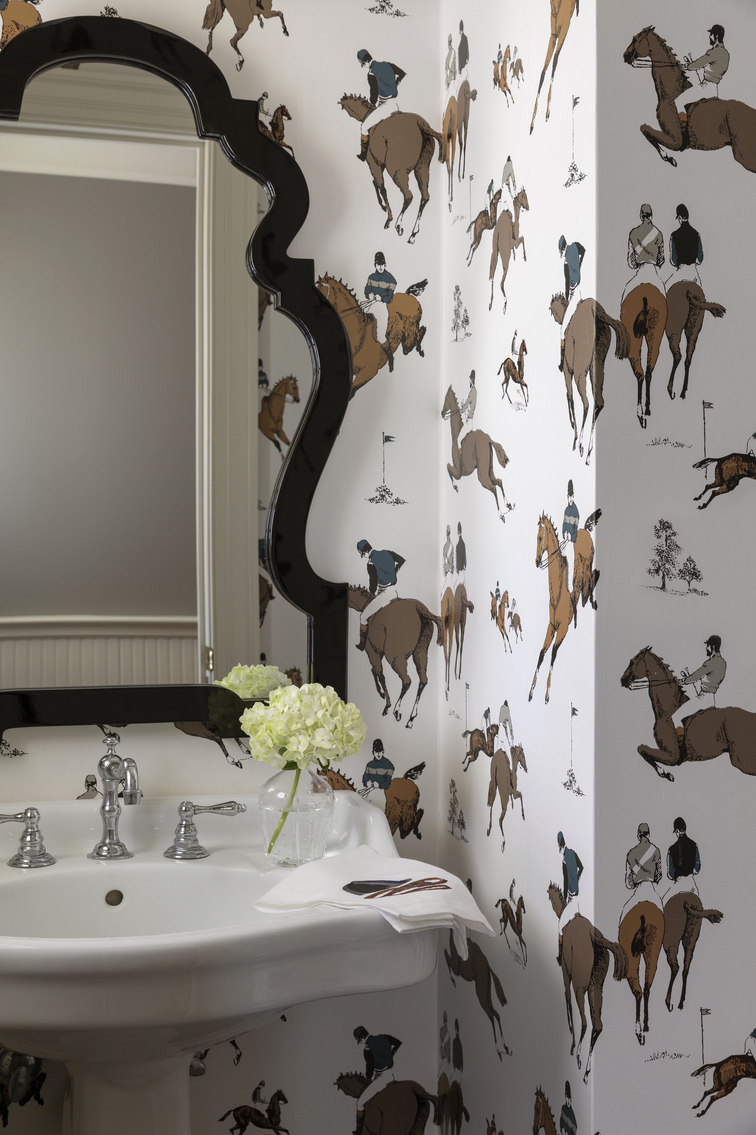 Bathroom with a white sink, silver fixtures, and a mirror. The wall has wallpaper with illustrations of people riding horses.