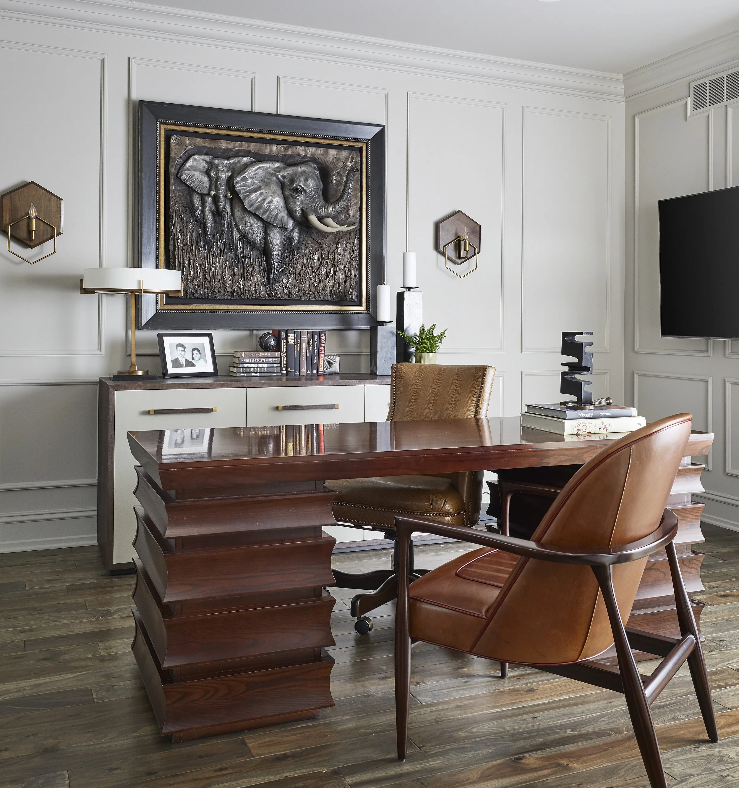 Modern living room with a wooden table, leather chairs, wall art of an elephant, books, framed photo, and decorative items.