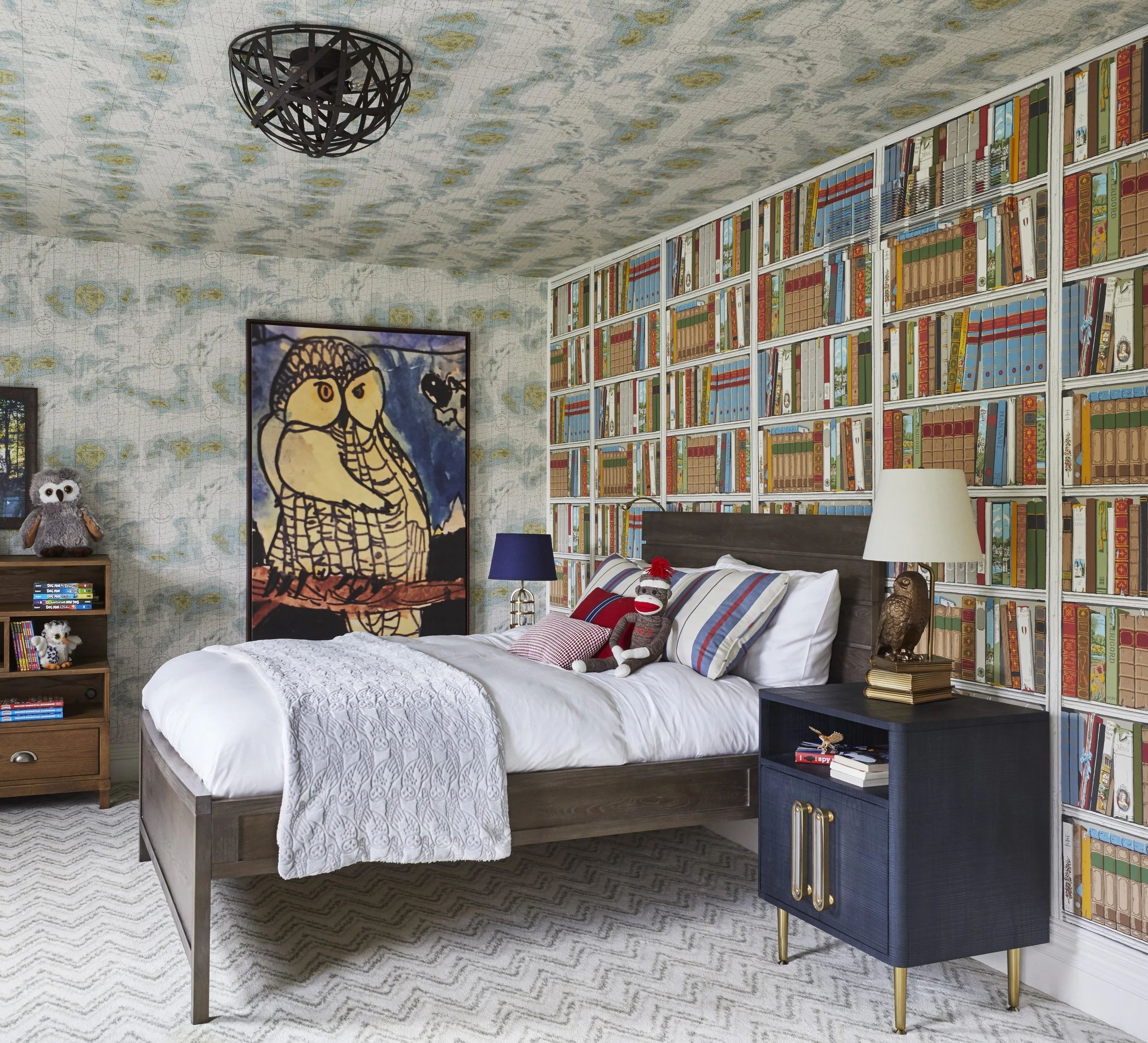 A cozy bedroom with a white bed, bookshelf filled with books, wall art, and plush toys.