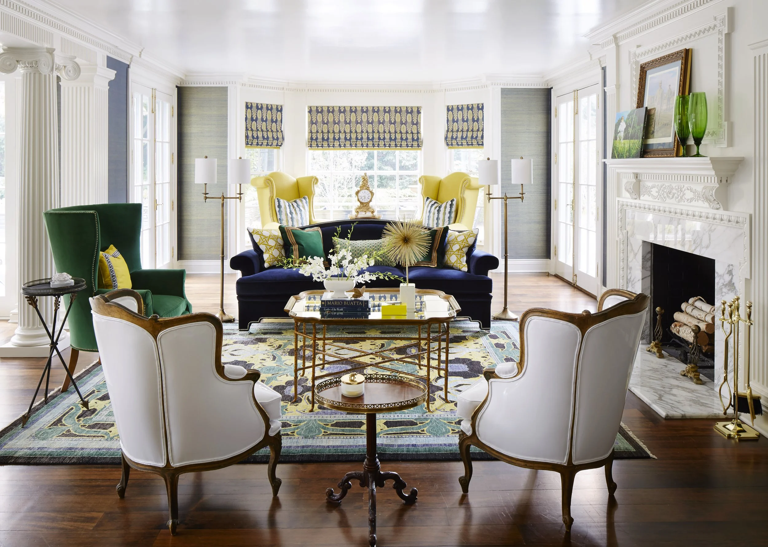 Bright living room with colorful furniture and decorative accents, including a white fireplace, framed artwork, green vase, and a mix of chairs and a sofa.