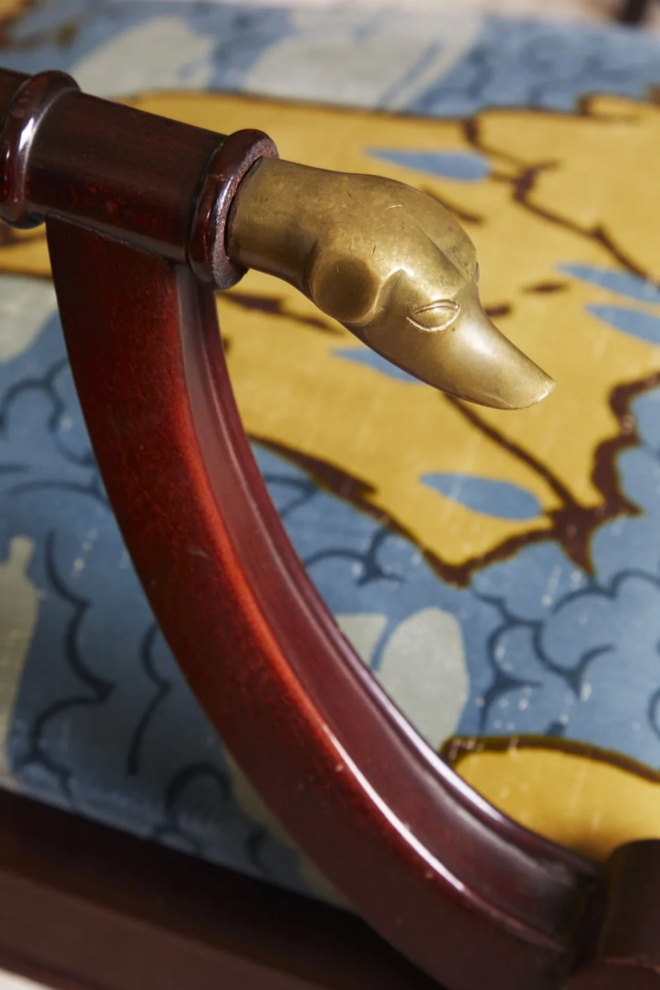 Close-up of a decorative wooden frame with a brass duck's head carving at the corner, set against a background of a painted wooden surface.
