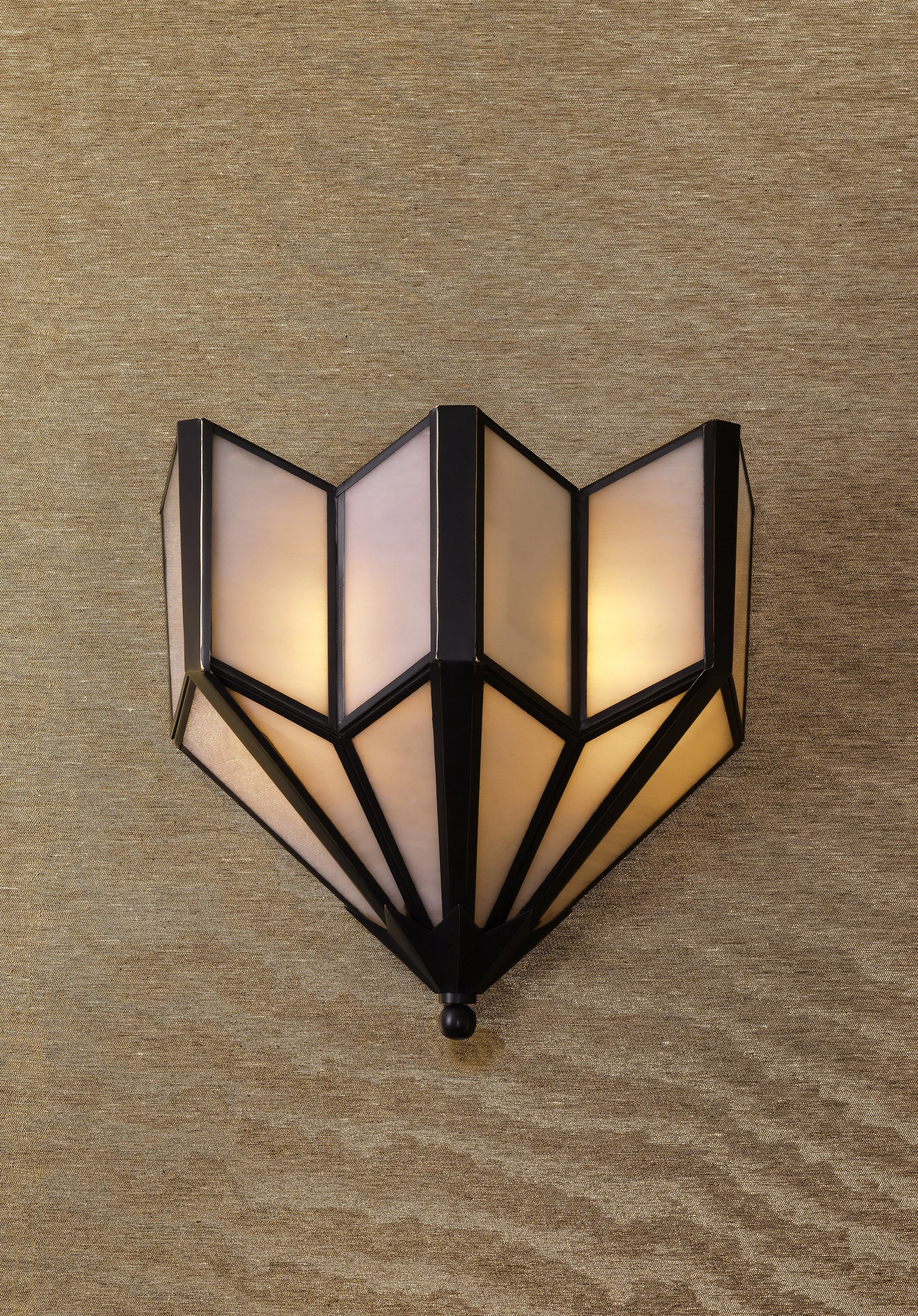 A black and white geometric wall sconce with illuminated white panels, mounted on a gold textured wall.