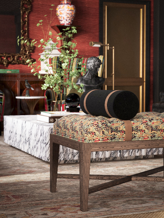 A living room with a wooden bench topped with a colorful floral cushion and a black and tan cylindrical pillow. In the background, there is a marble coffee table, a tall plant, a framed mirror, and an ornate carved mirror on the red wall.