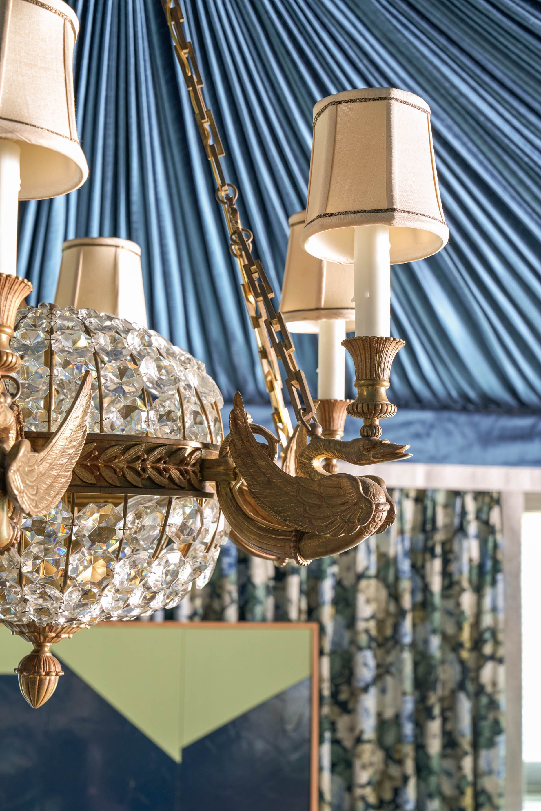Close-up of a decorative chandelier with a gold peacock ornament and a crystal globe, set against a blue curtain backdrop.
