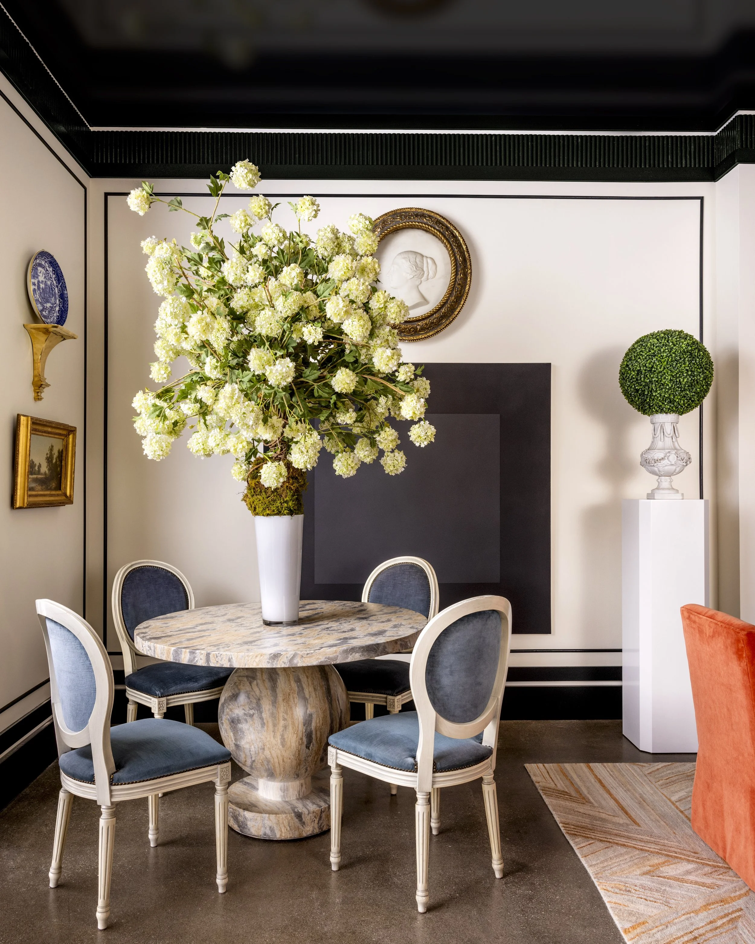A round marble table with four white and blue upholstered chairs in a room decorated with floral art and vintage decor.