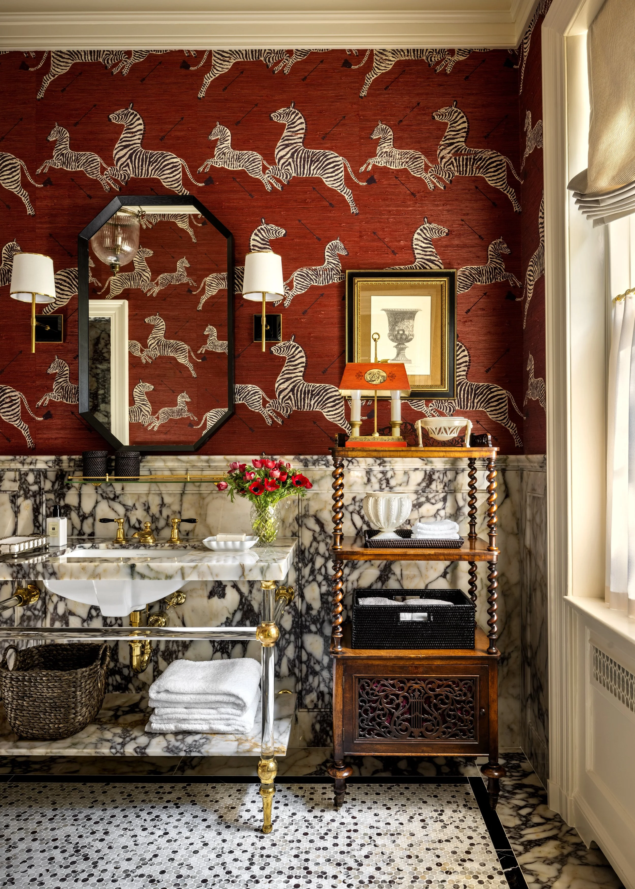 A luxurious bathroom with a marble sink, a wooden cabinet, and decorative wall art featuring zebras and arrows on a red wall.