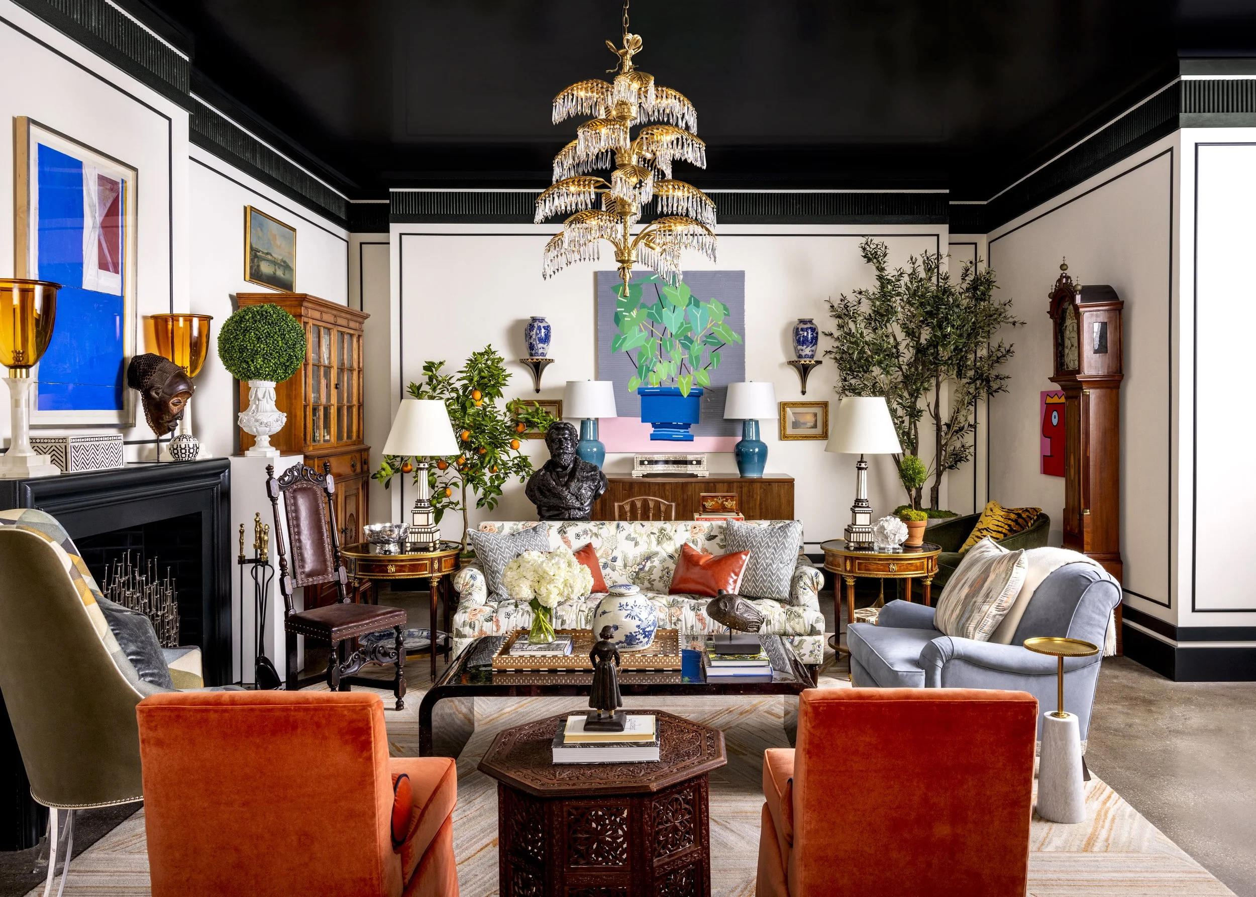 A living room with various colorful furniture and decorations, including a chandelier, paintings, plants, and a mix of chairs and sofas.