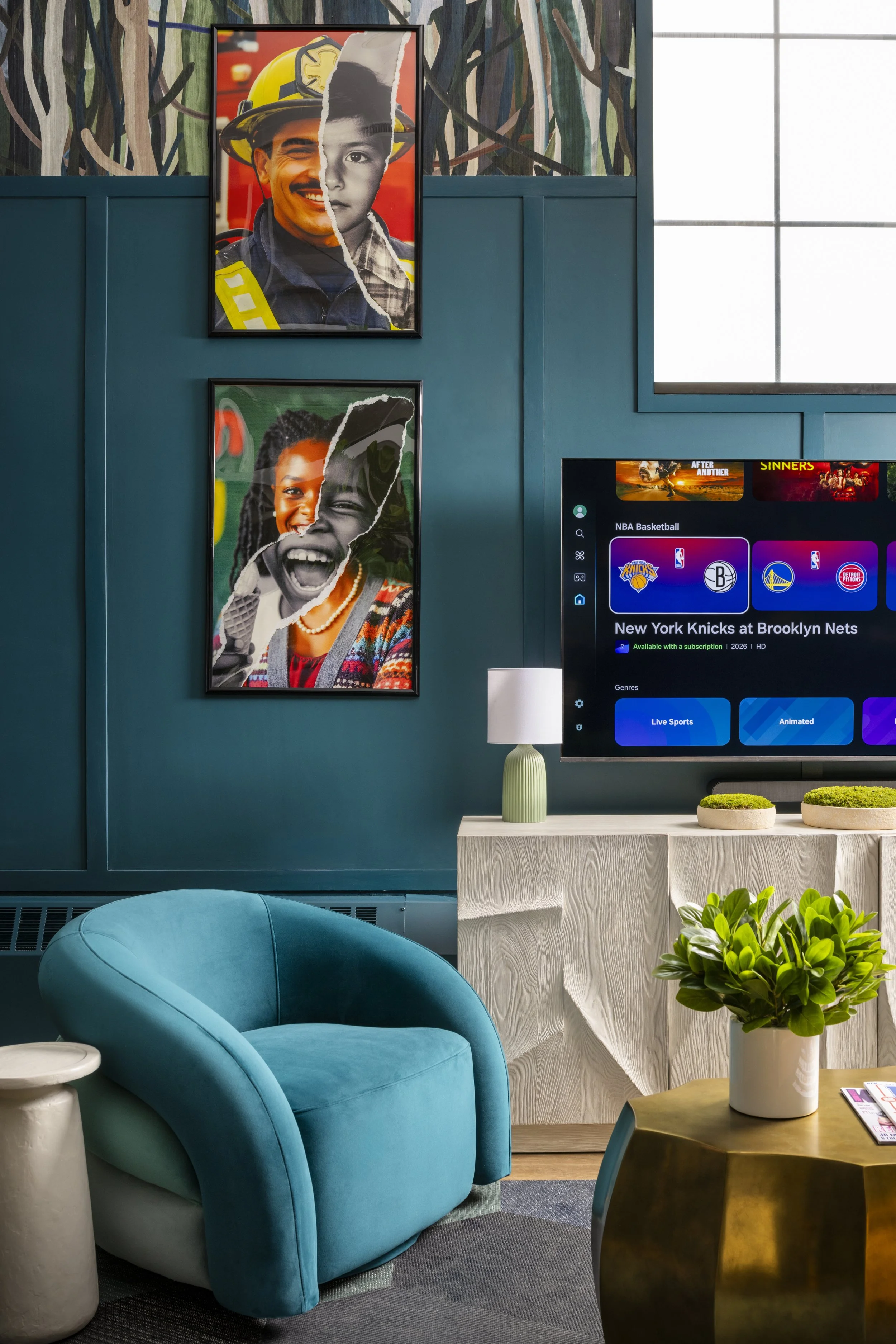 Modern waiting area with a teal velvet armchair, a gold side table with a white vase and green plant, white textured cabinet, wall art including two collage portraits of smiling children, a television displaying NBA basketball, a large window with gr