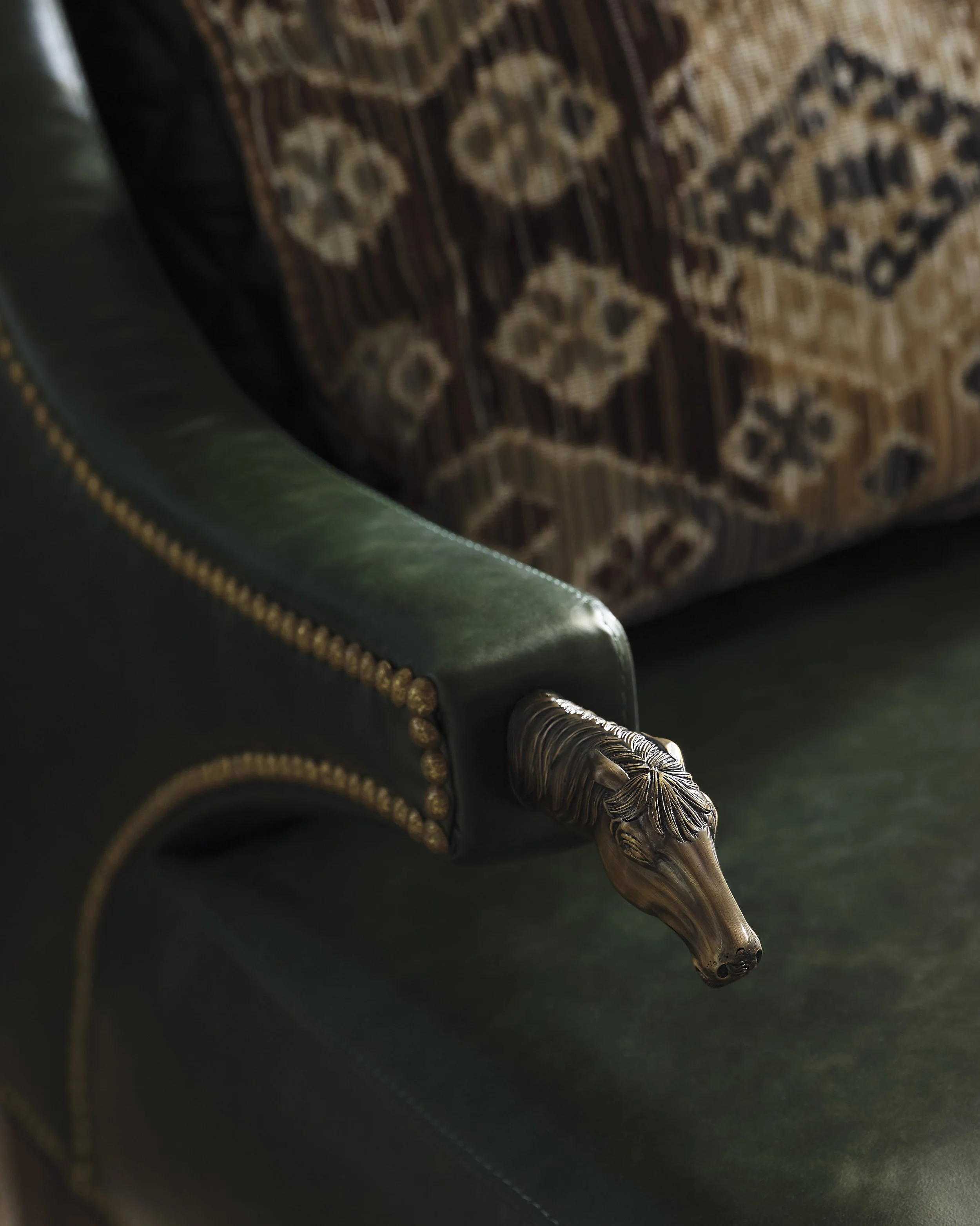 Close-up of a brass eagle-shaped pen attached to a dark green leather notebook, with a patterned carpet in the background.