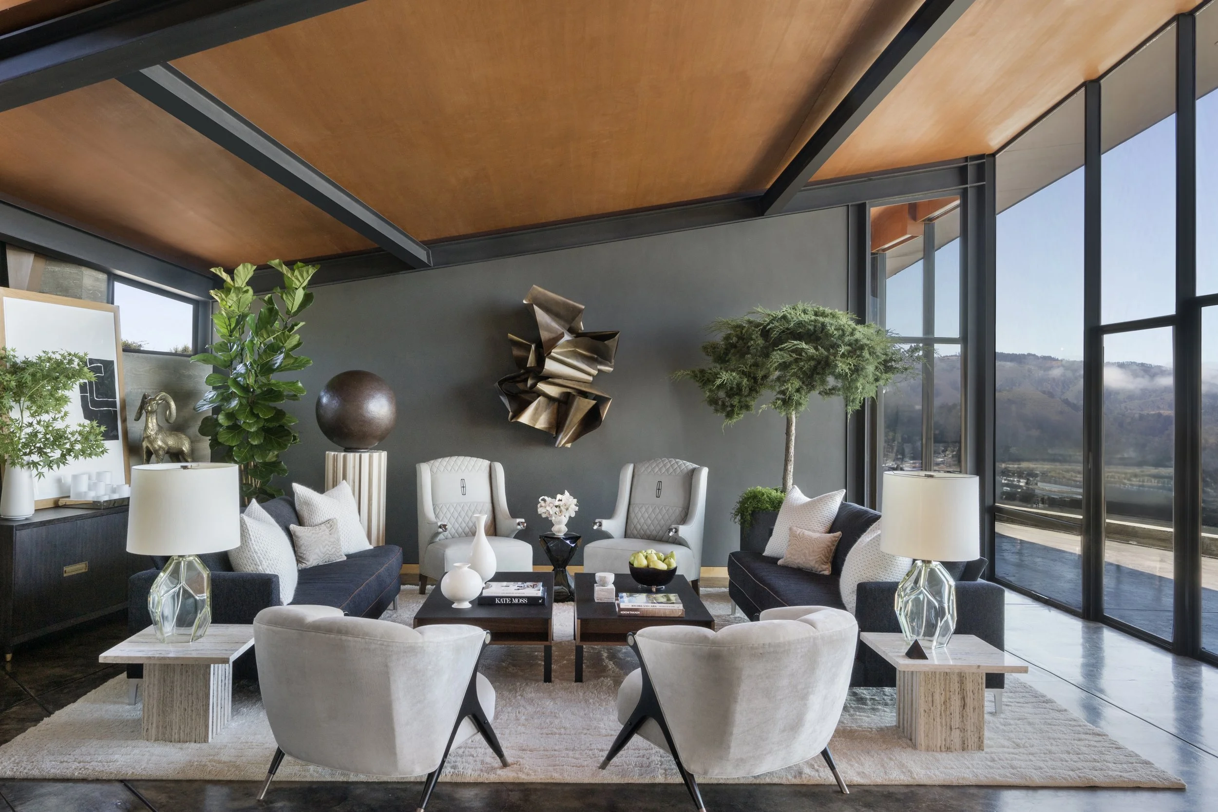 Modern living room with white, dark blue, and beige furniture, large windows, and indoor plants.