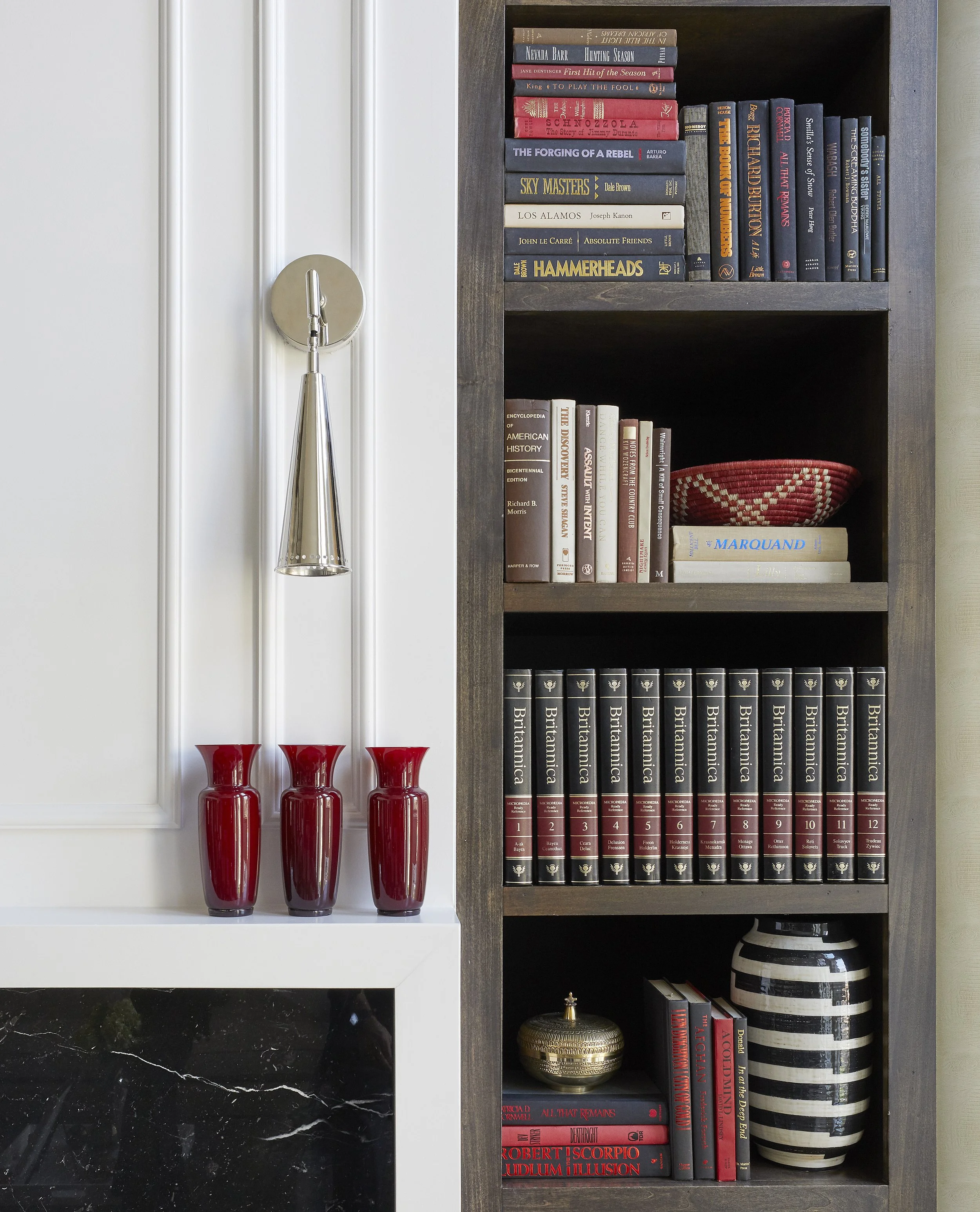 A bookshelf with multiple books organized vertically, with some titles including American history, classical literature, and academic topics, along with decorative vases and a small round metallic container.