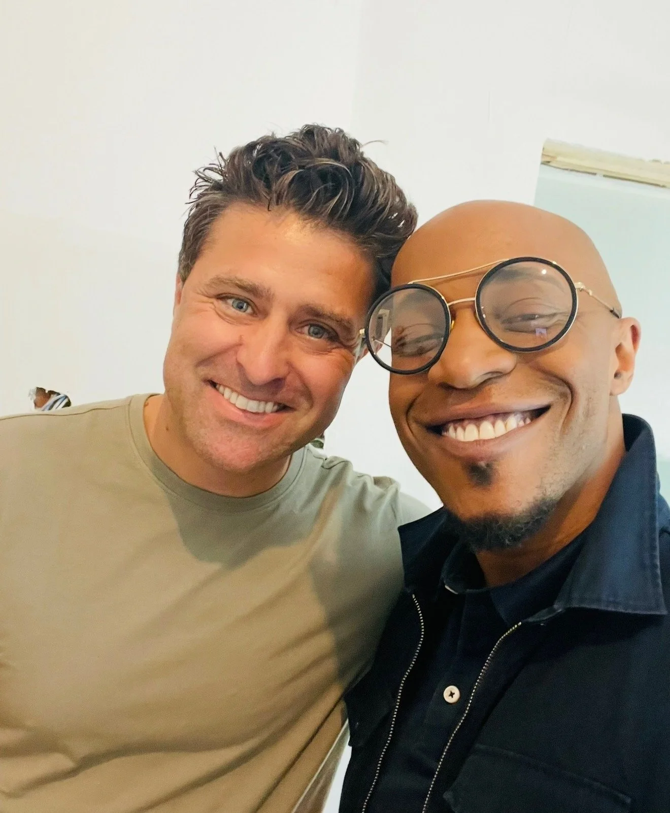 Two men taking a close-up selfie, smiling and posing together in an indoor setting.