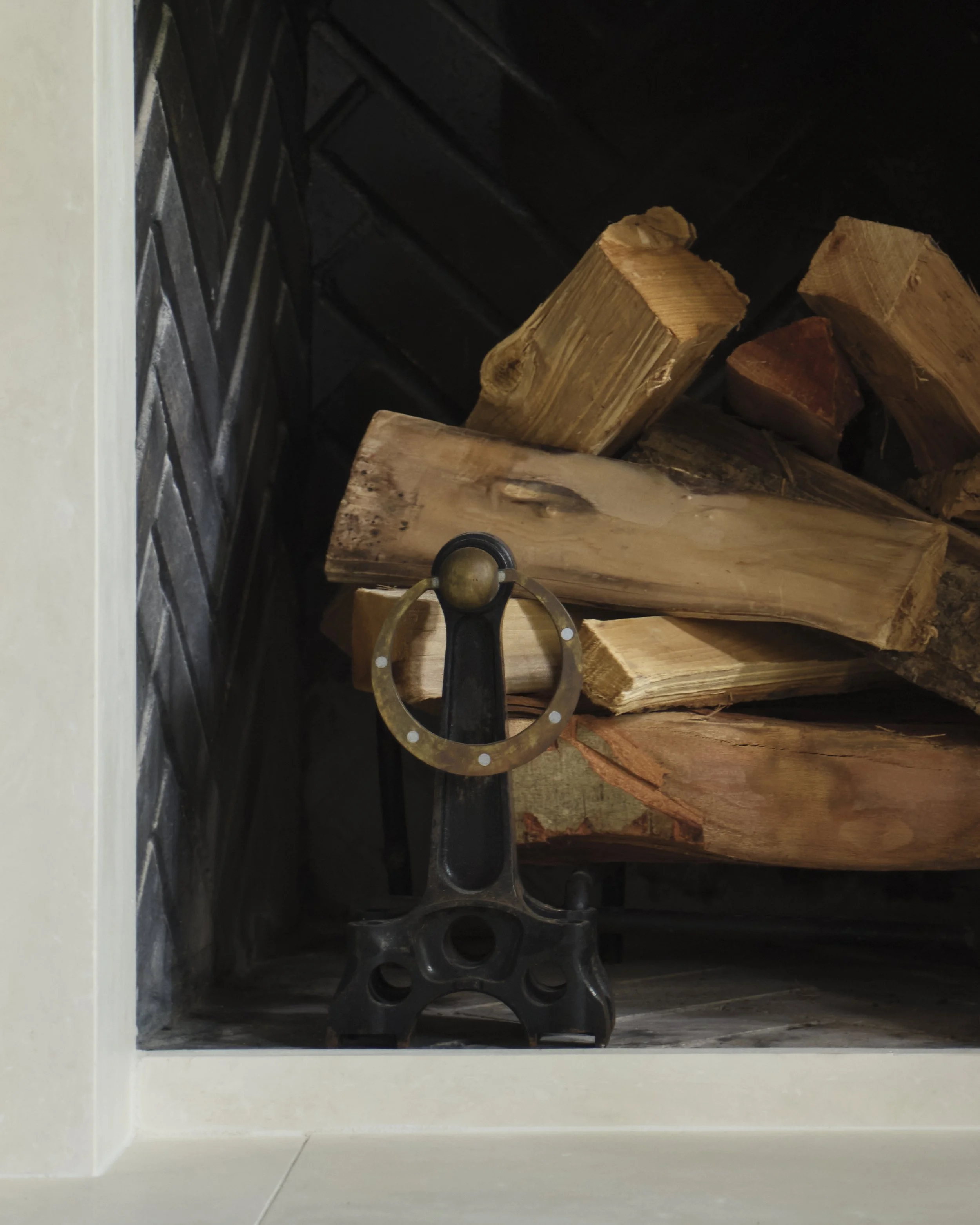 Firewood stacked inside a white fireplace or firewood storage with a metallic tool hanging in front.