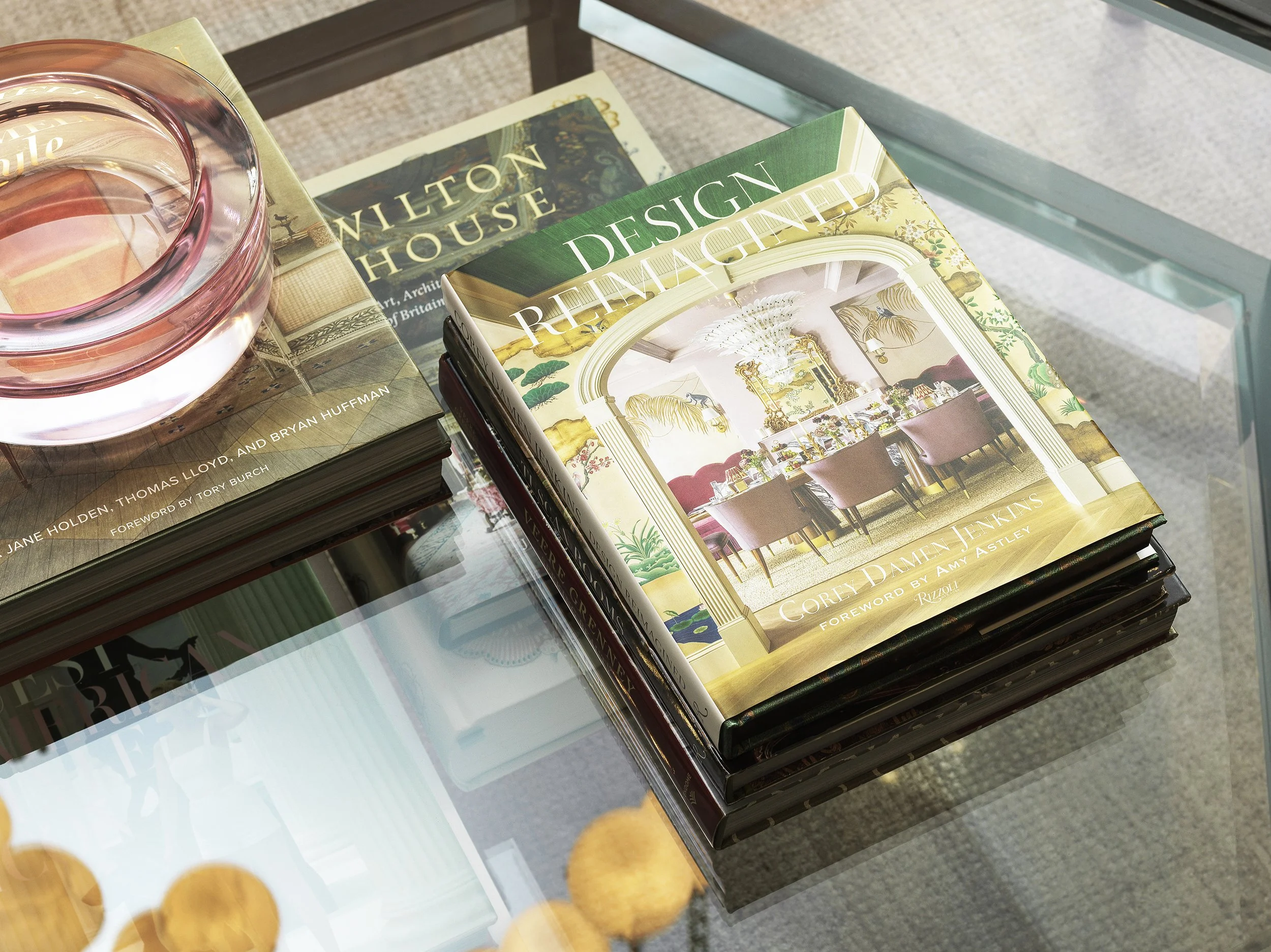 A glass table with several architecture and interior design books stacked on it, and a glass of water placed on top of one of the books.