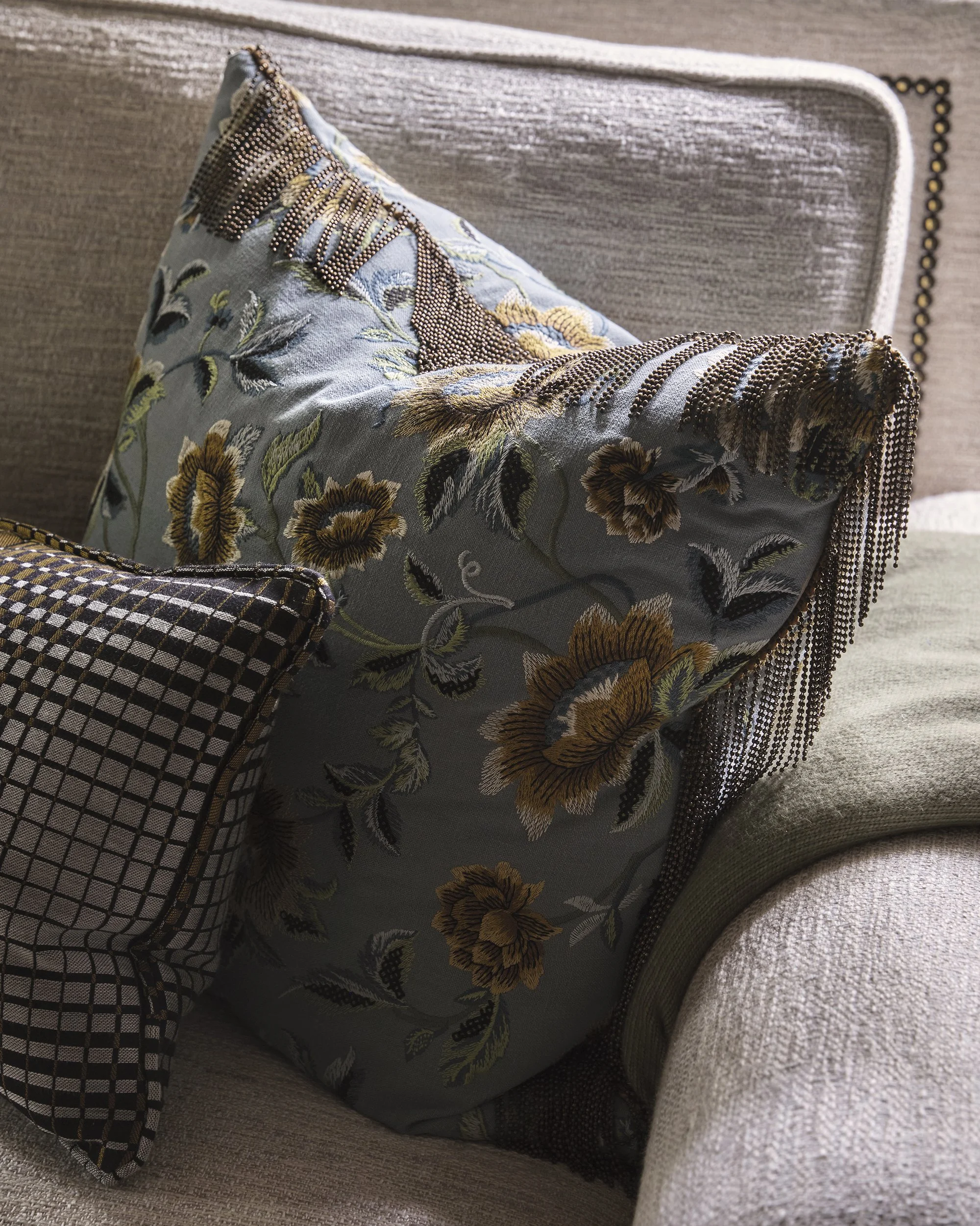 Close-up of a floral embroidered pillow with bead detailing, sitting on a textured beige armchair.