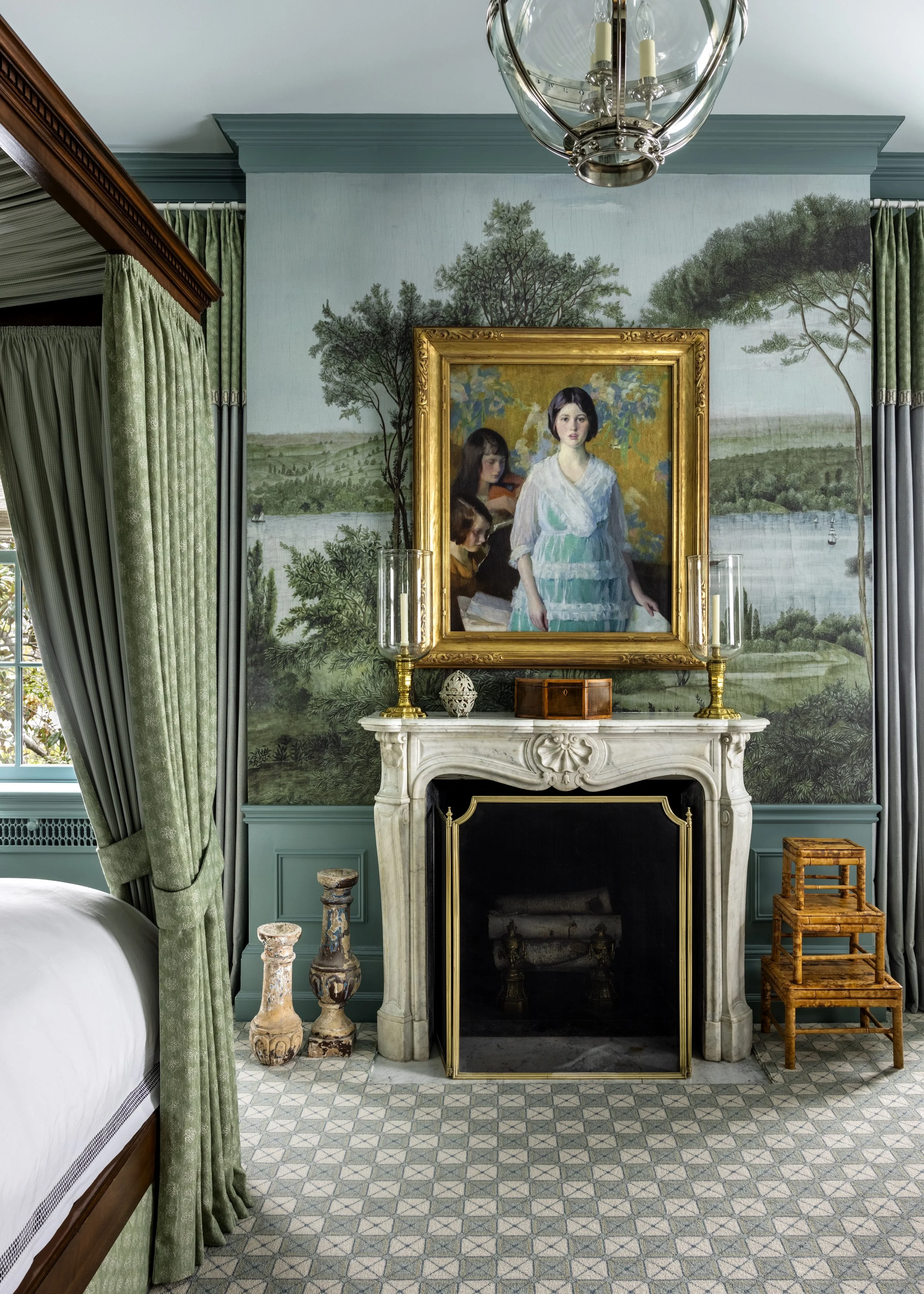 Interior of a room with a marble fireplace, green drapes, twin candlesticks with glass hurricane covers, a painting of three women in a landscape, and patterned tile flooring.
