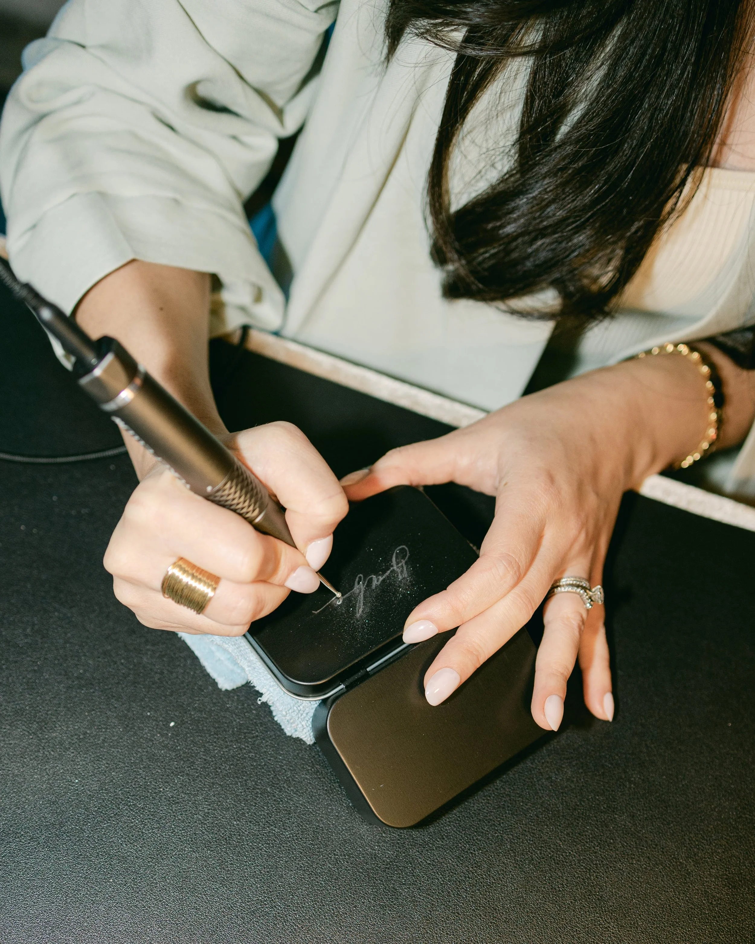 Person using a laser engraver to personalize a black phone case with a signature or design.