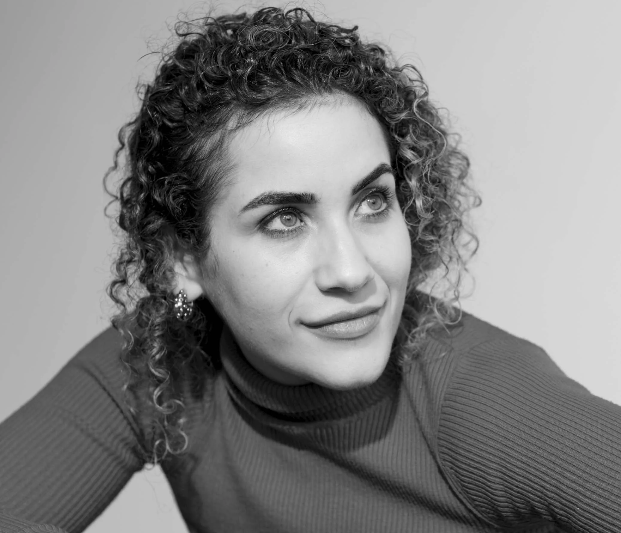 Black and white close-up portrait of a woman with curly hair and light-colored eyes, looking slightly away from the camera.