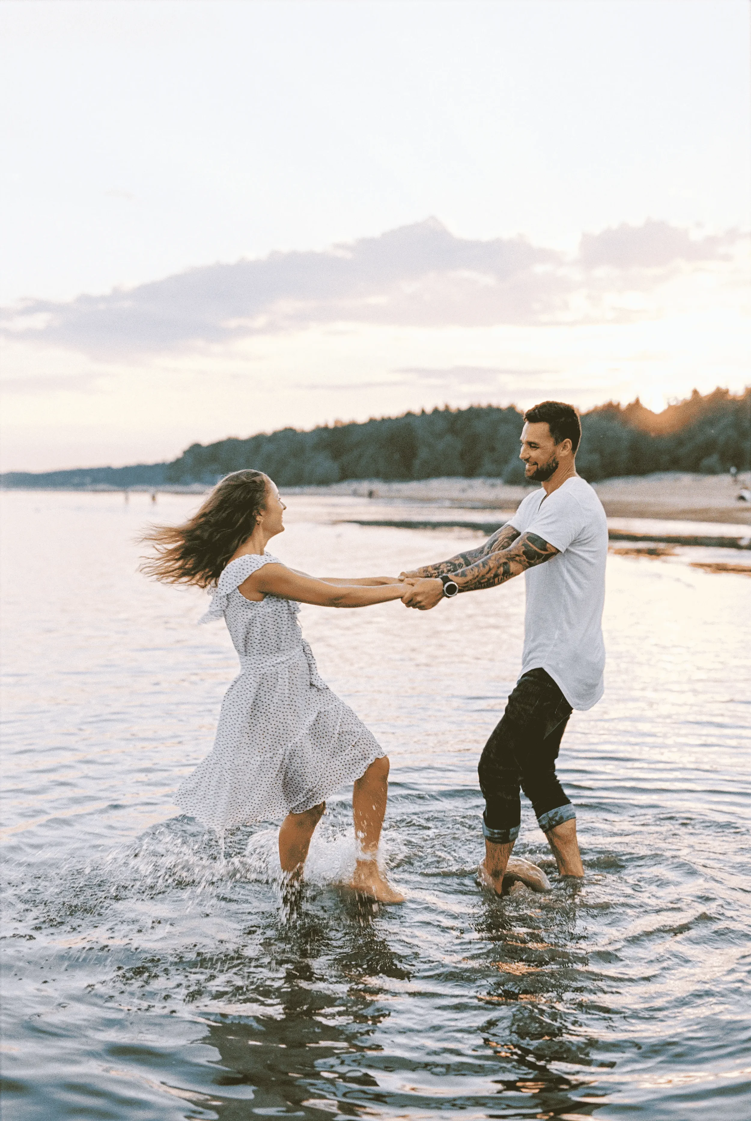 A happy couple walking hand in hand through clear, shallow water, representing somatic couples therapy.