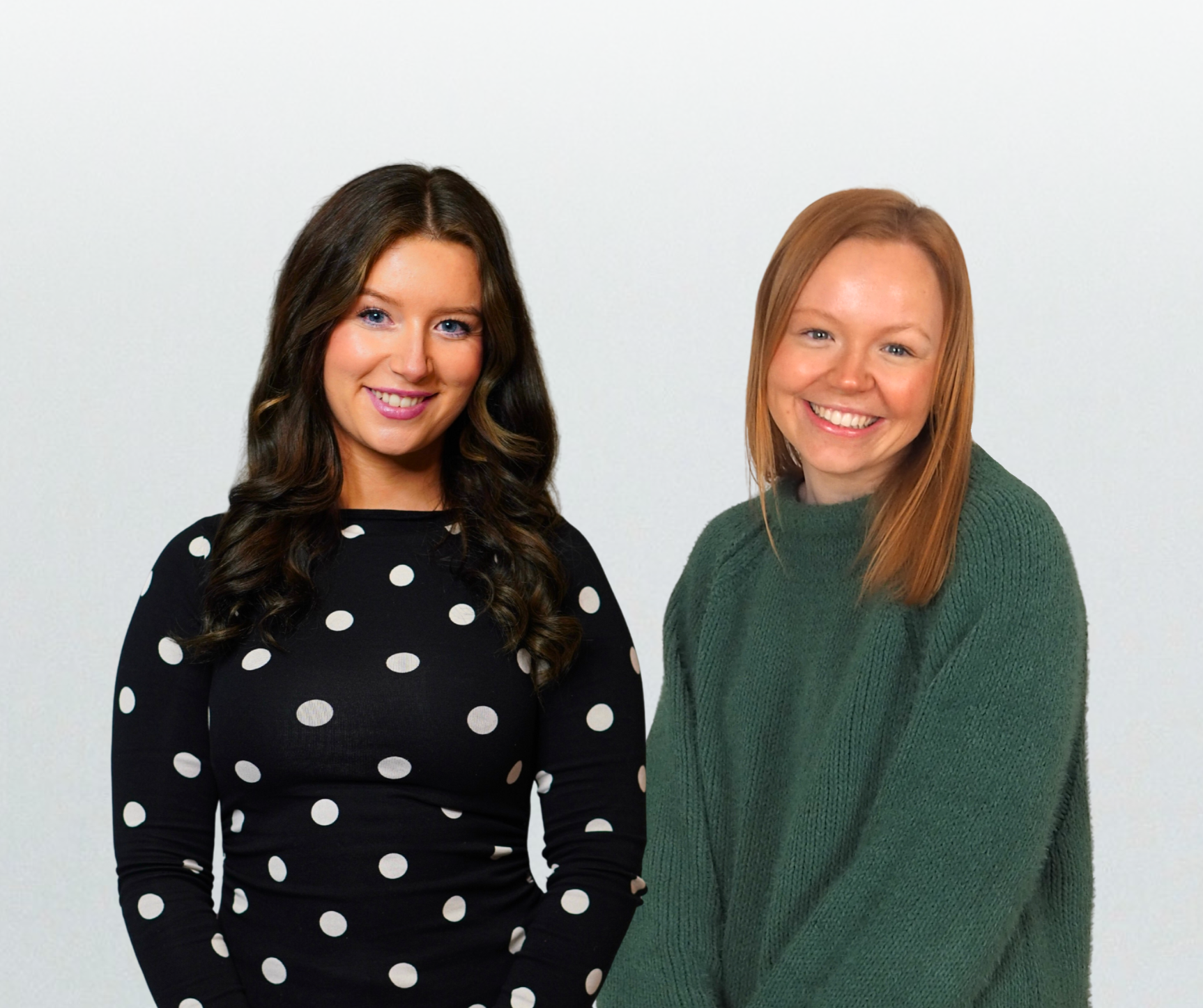 Two women standing side by side, smiling at the camera, against a plain white background.