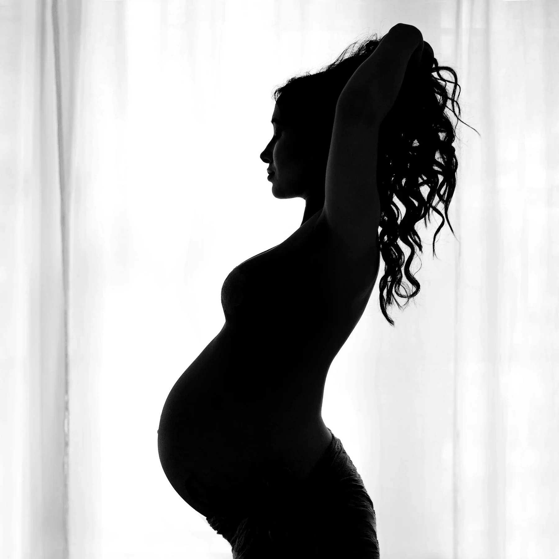 A maternity silhouette against a softly lit curtain