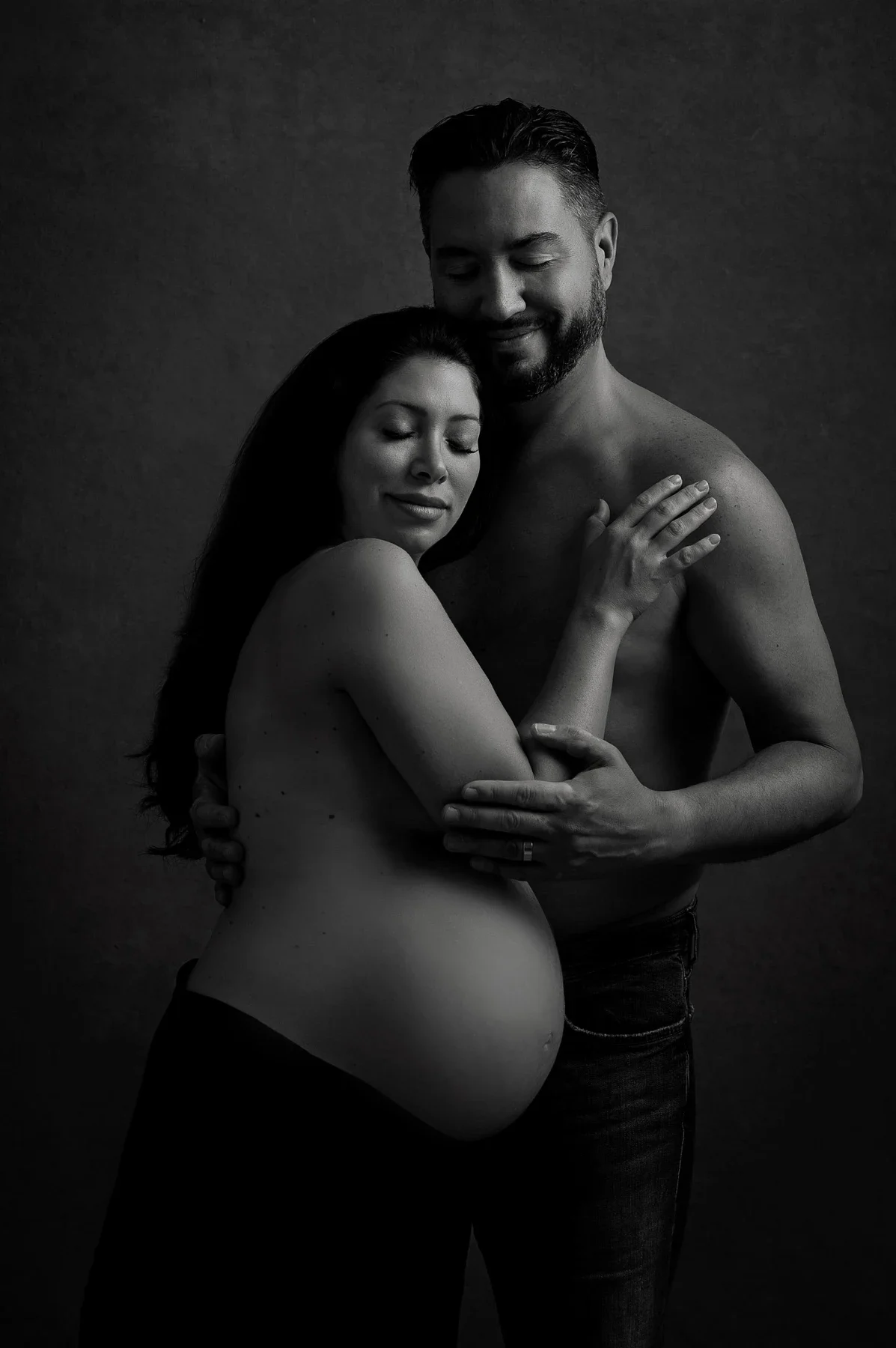 An expectant couple sharing a quiet embrace in black and white