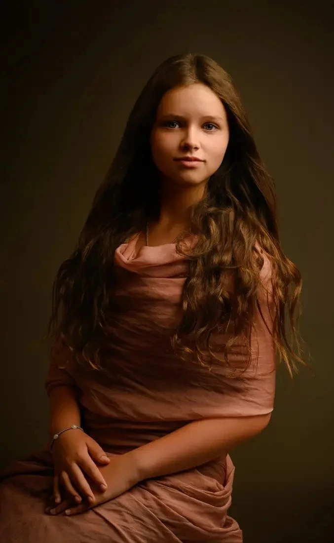 A child in a rose-colored draped gown seated with composed posture in a fine art portrait