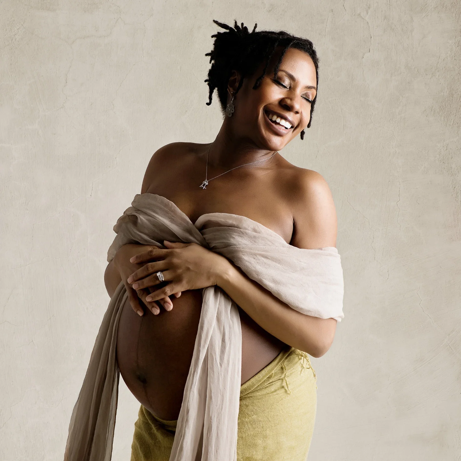 An expectant mother smiling freely in soft draped fabric
