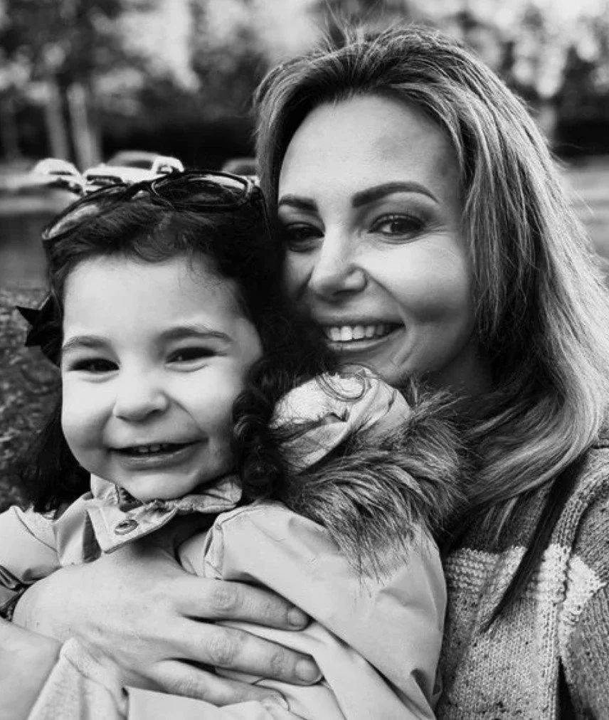 Black and white photo of a woman and a young girl smiling and hugging outdoors.
