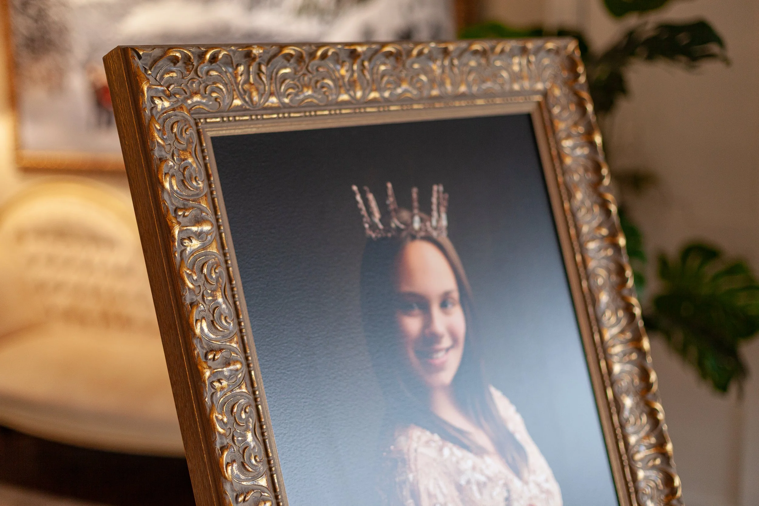 A framed portrait of a woman wearing a crown with spikes, smiling, with dark hair and light-colored clothing, in a decorative gilded frame.