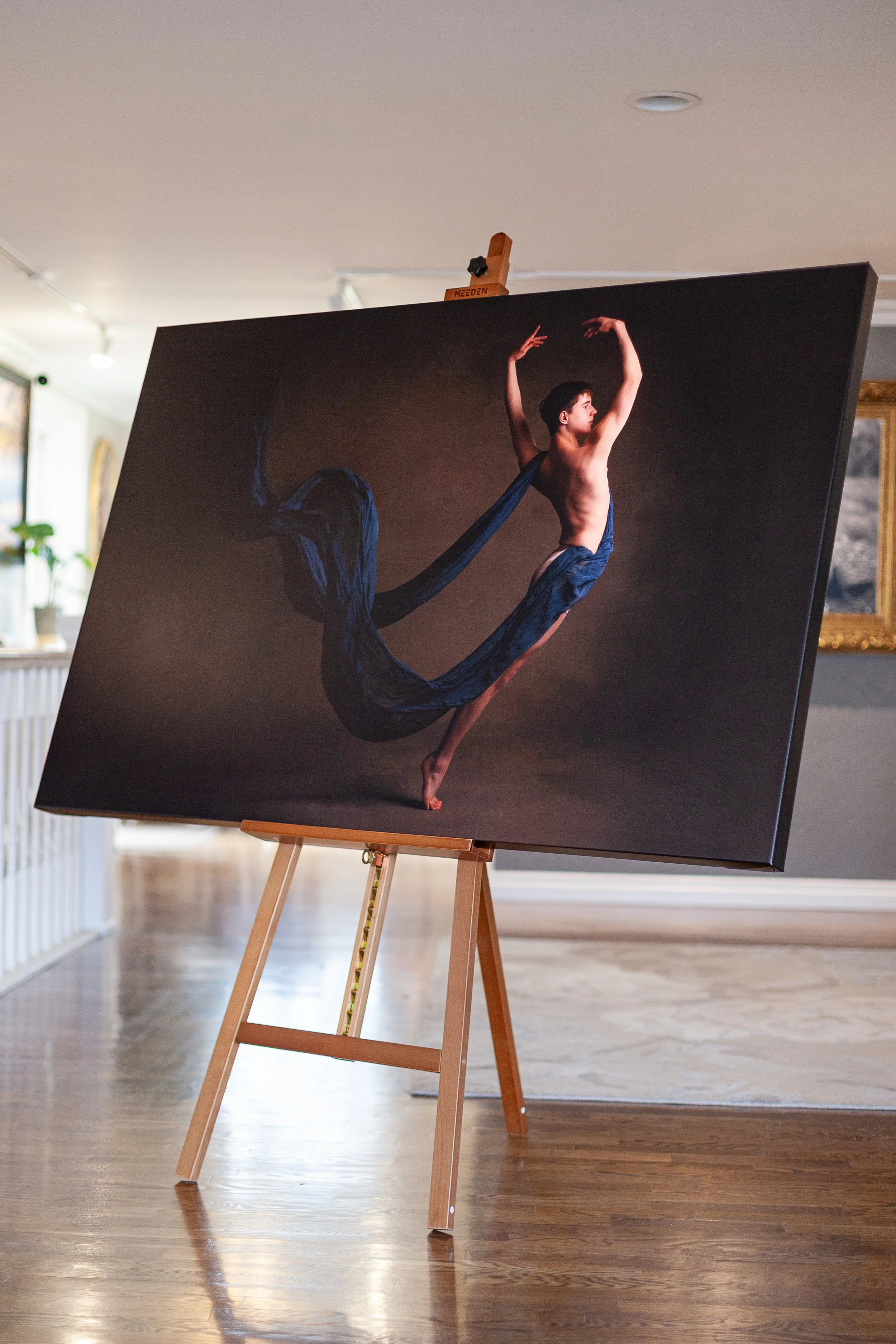 Painting of a ballet dancer in a dark background, wearing a flowing blue dress and posing with arms up and one leg extended.