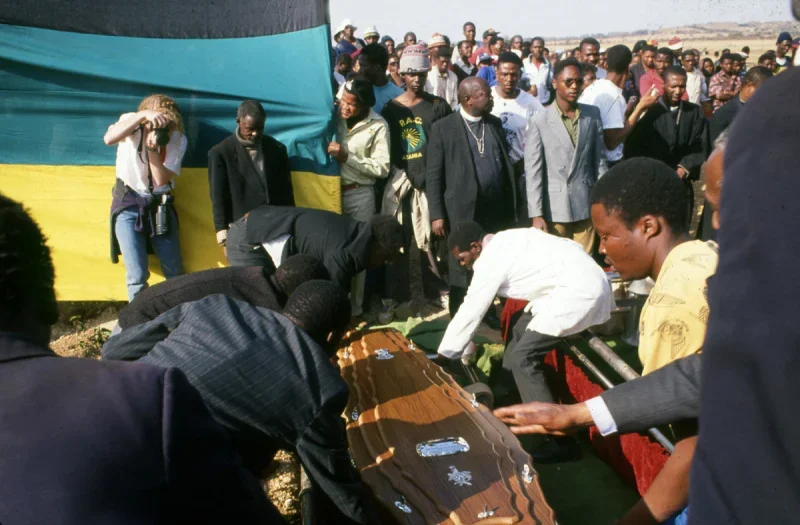 People gather around a coffin draped with a flag, participating in a funeral or memorial service.