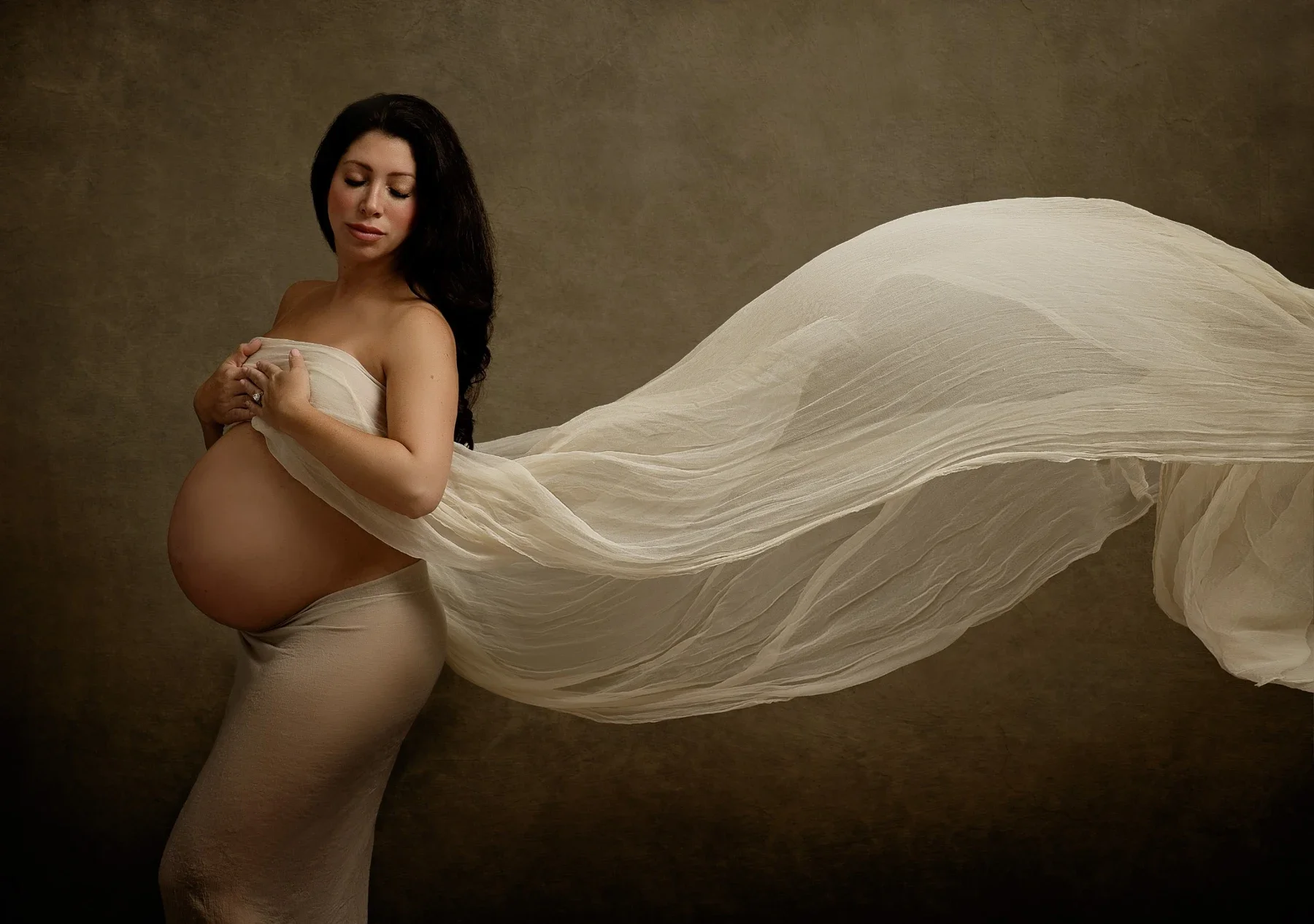 An expectant mother with flowing ivory fabric against a warm painted backdrop