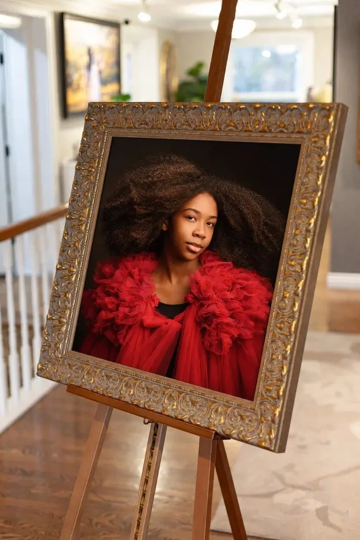 An ornate framed portrait of a child in red displayed on an easel in the studio