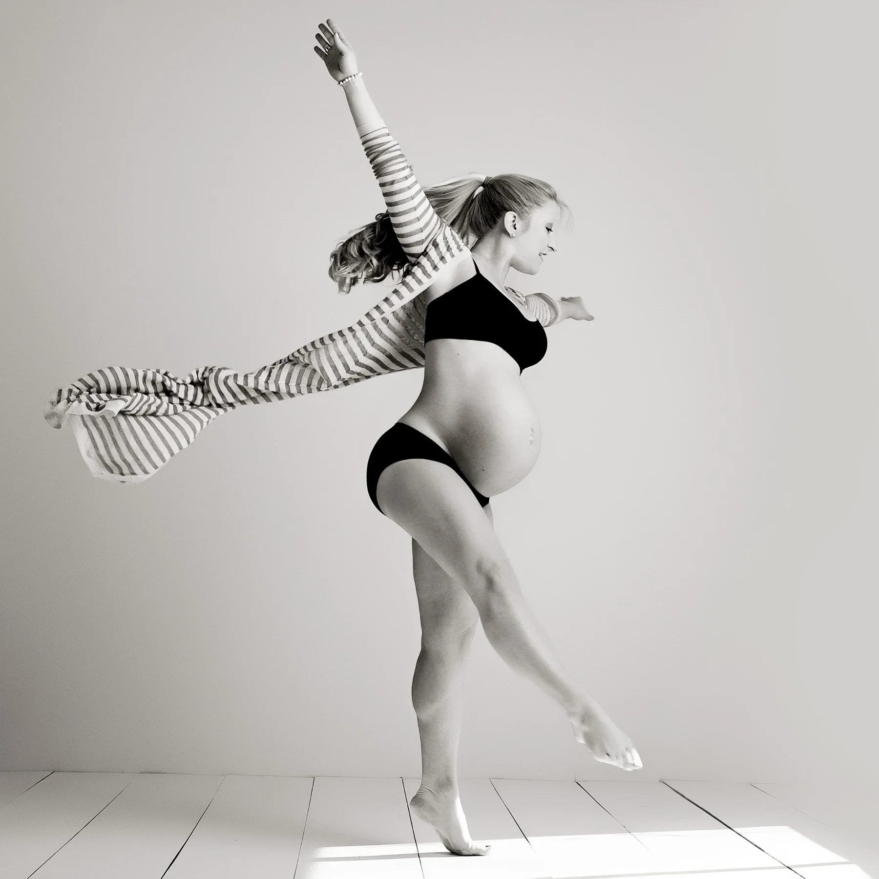 A pregnant dancer extending her arms in a sunlit studio