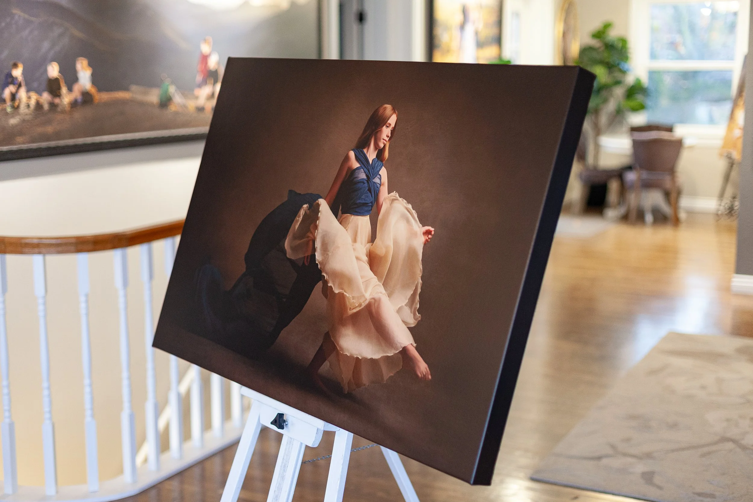 A photograph of a woman in ballet attire, captured on a large easel in an art gallery. The magazine-like photo is prominently displayed with a blurred background of an elegant room with hardwood floors and large windows.