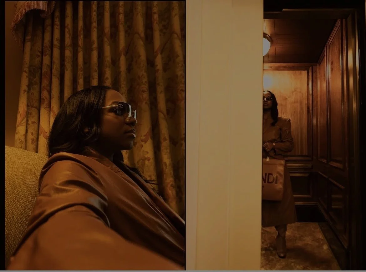 A woman sitting in a room with patterned curtains, wearing sunglasses and a brown satin jacket, and another woman standing in a wood-paneled hallway, partially obscured by a wall, holding a brown shopping bag.