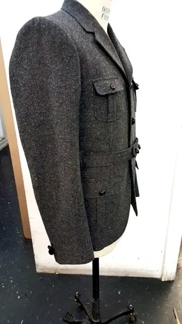 Black textured blazer, featuring a notched lapel, flap pockets, and a waist belt with a buckle.