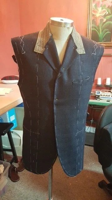 A dress form with a partially sewn dark fabric garment, featuring a contrasting patterned collar.