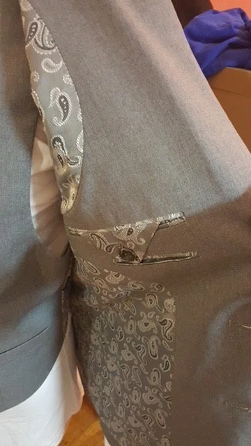 Close-up of a gray vest with paisley pattern details and a clasp