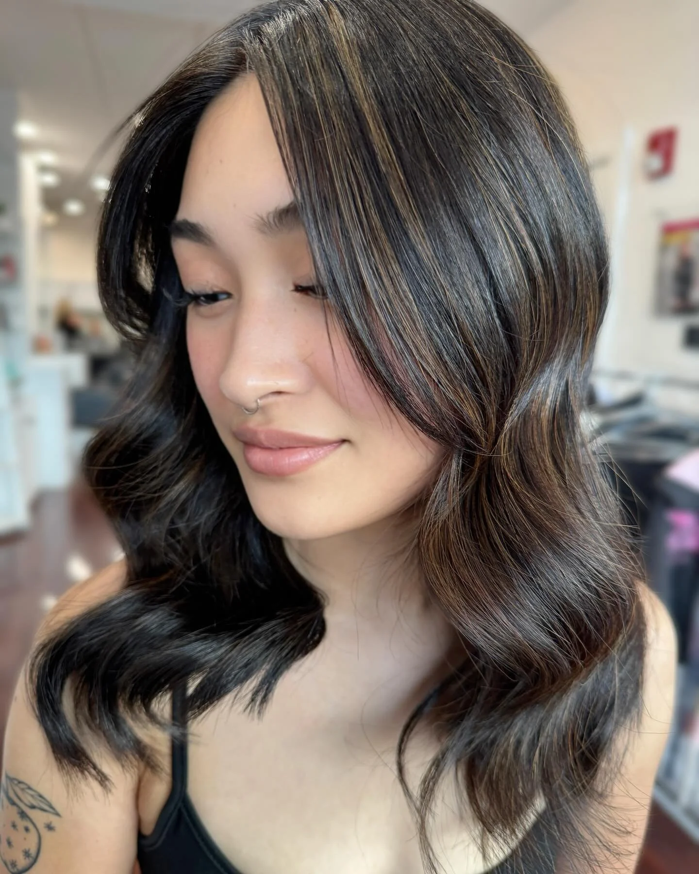 Close-up of a woman with styled black hair with brown highlights, smiling softly with closed eyes, in a salon setting.