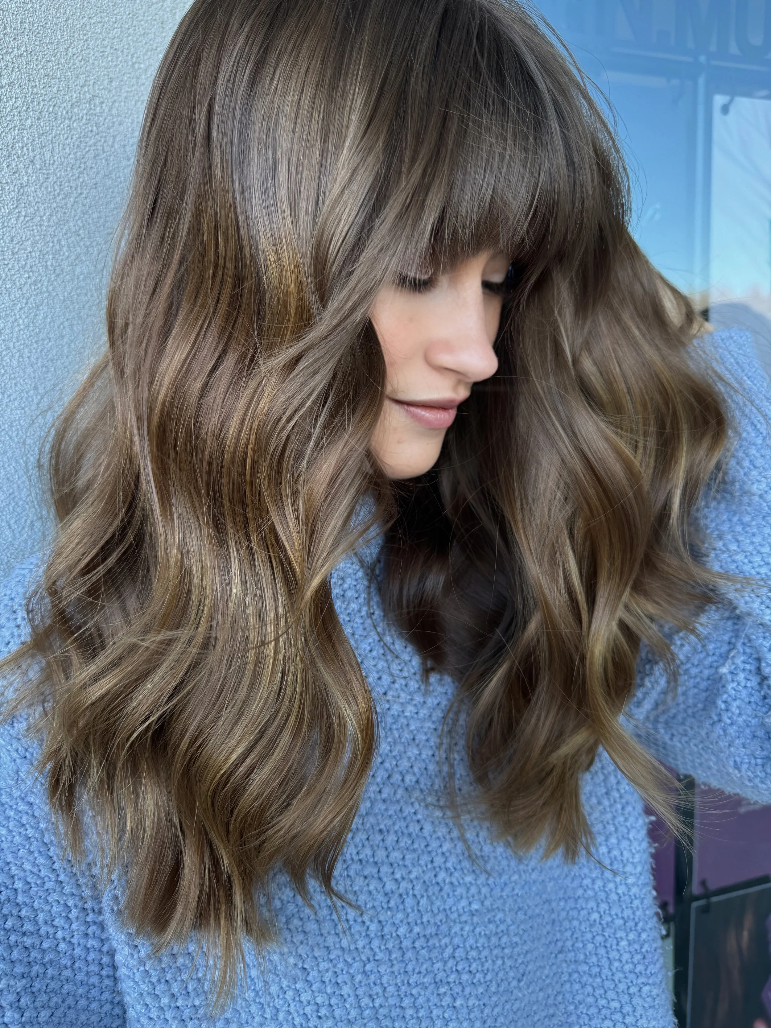 Close-up of a young woman with long, wavy, light brown hair wearing a textured blue sweater.
