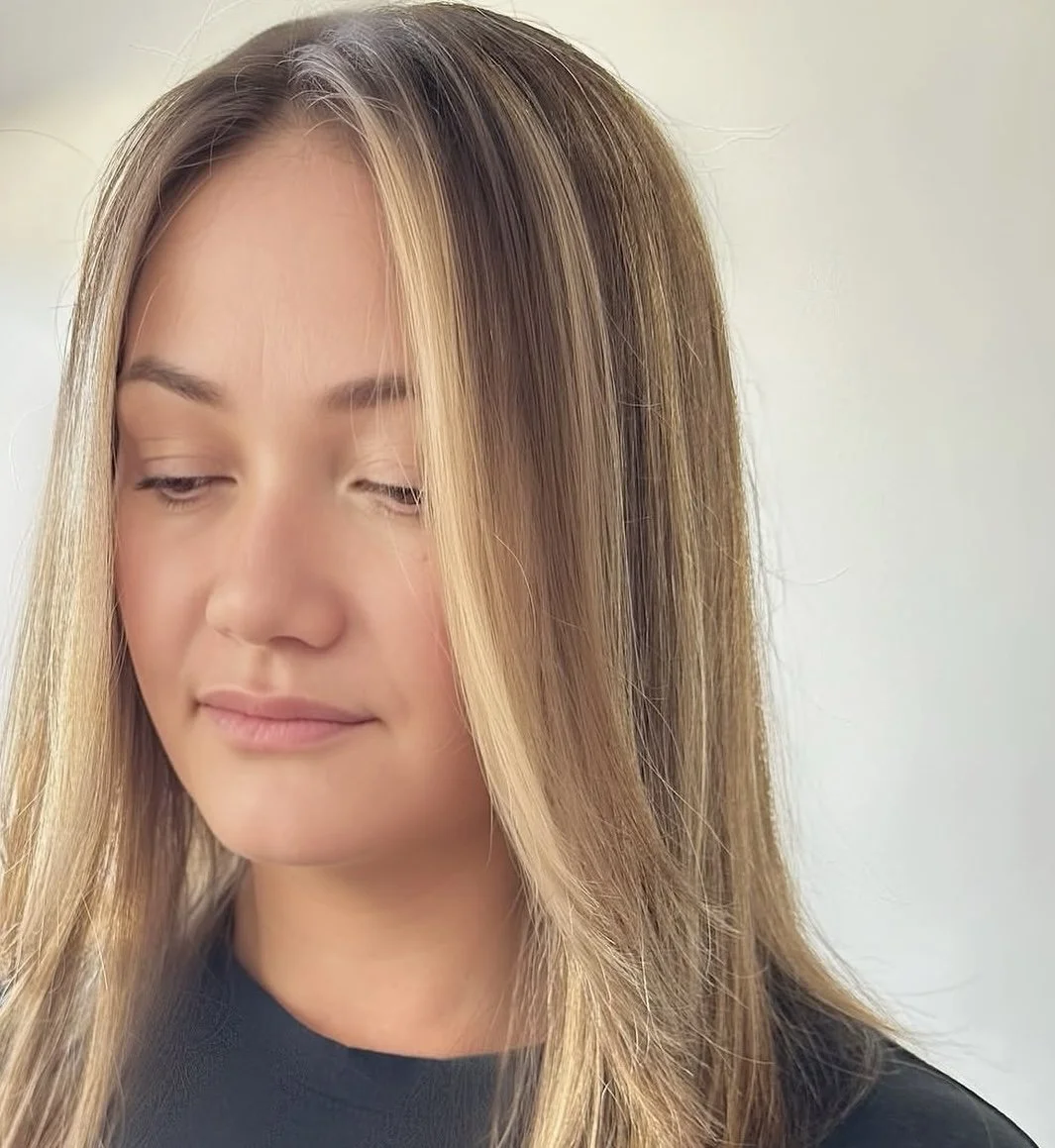 Close-up of a young woman with blonde hair, looking downward with a gentle expression, against a neutral background.