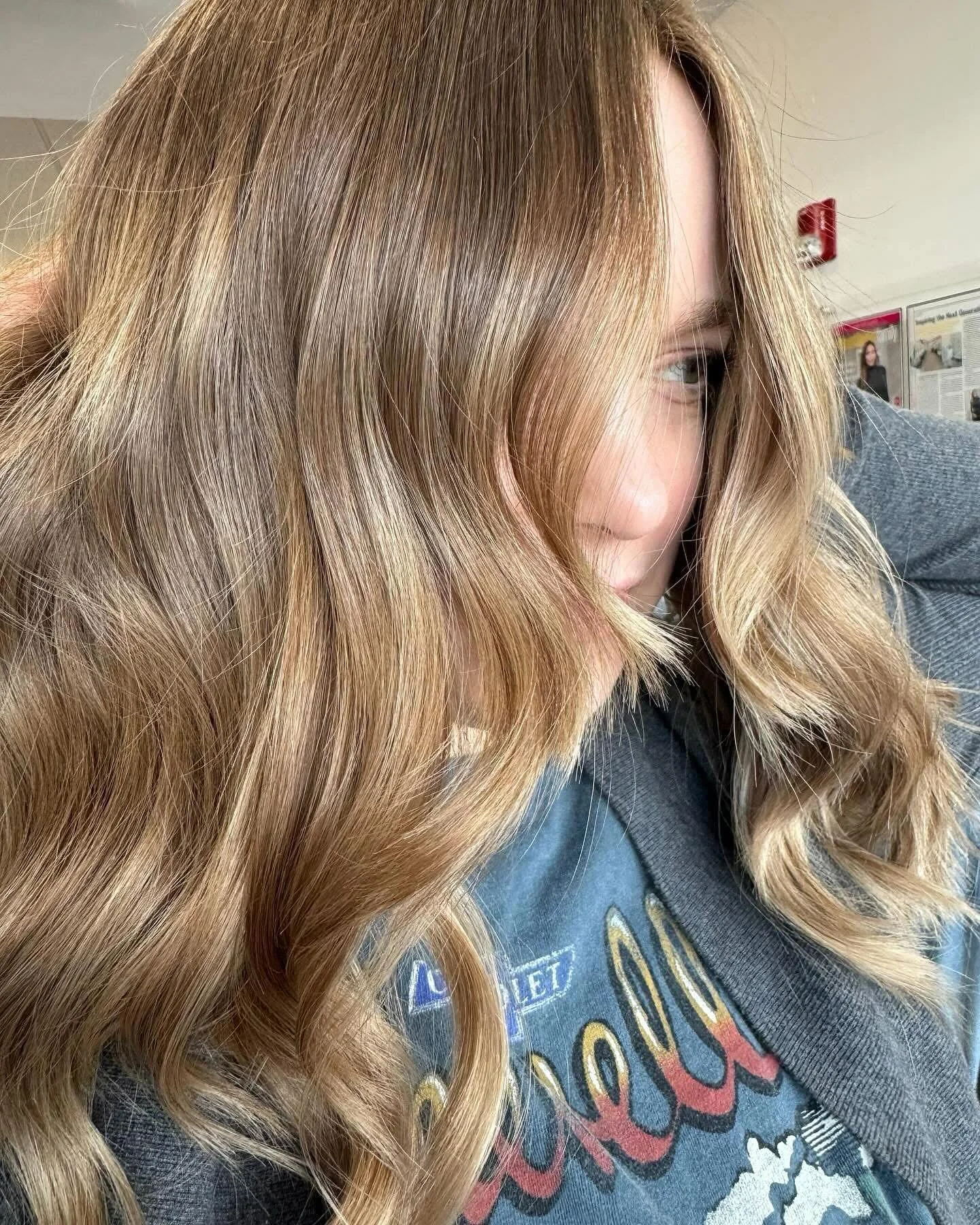Close-up of a woman with long, wavy blonde hair partially covering her face, wearing a dark shirt with a graphic print.