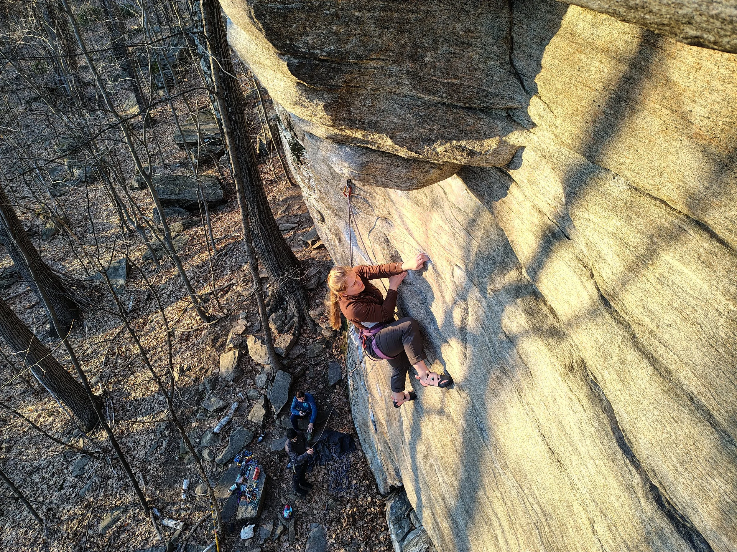 A woman rock climbing on a vertical outdoor cliff, using climbing gear and safety ropes.